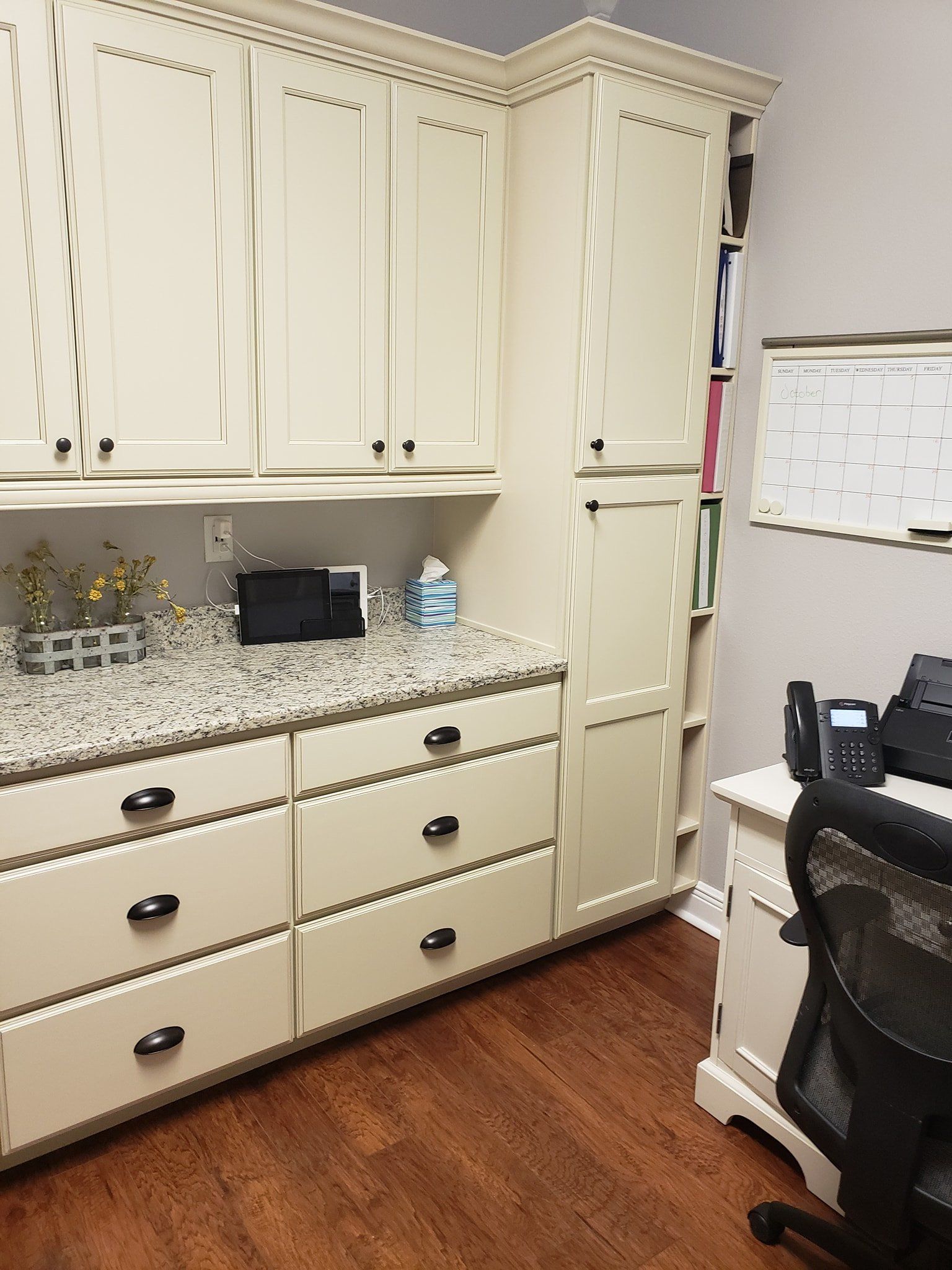 A home office featuring off-white cabinetry, a granite countertop, and a white desk with a chair and desk phone.
