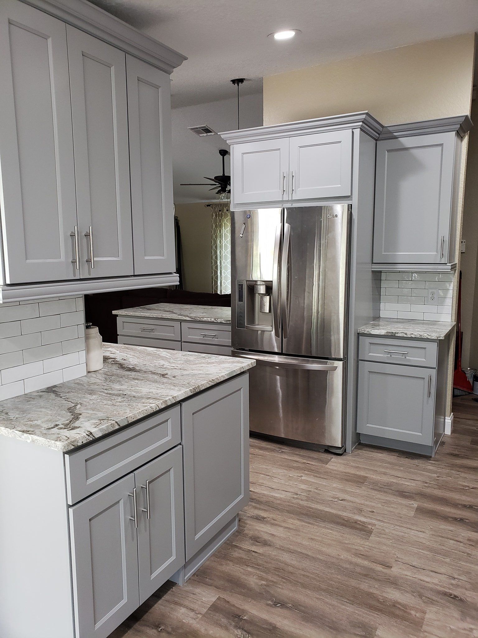 Modern kitchen featuring light gray cabinets, white granite countertops, stainless steel appliances, and wood floors.