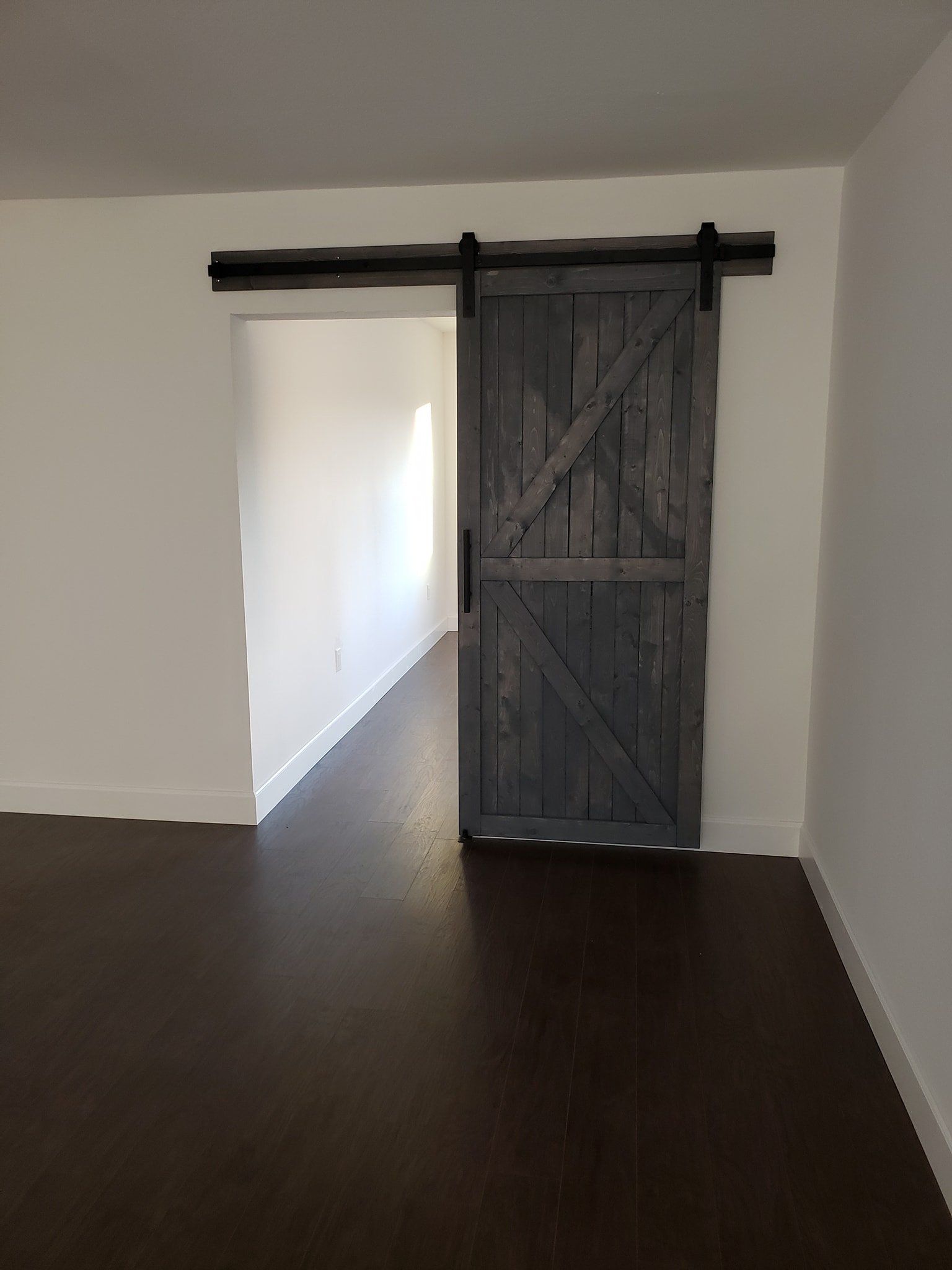 A grey wooden barn-style sliding door with black hardware, mounted in a doorway between a dark wood floor and white walls.