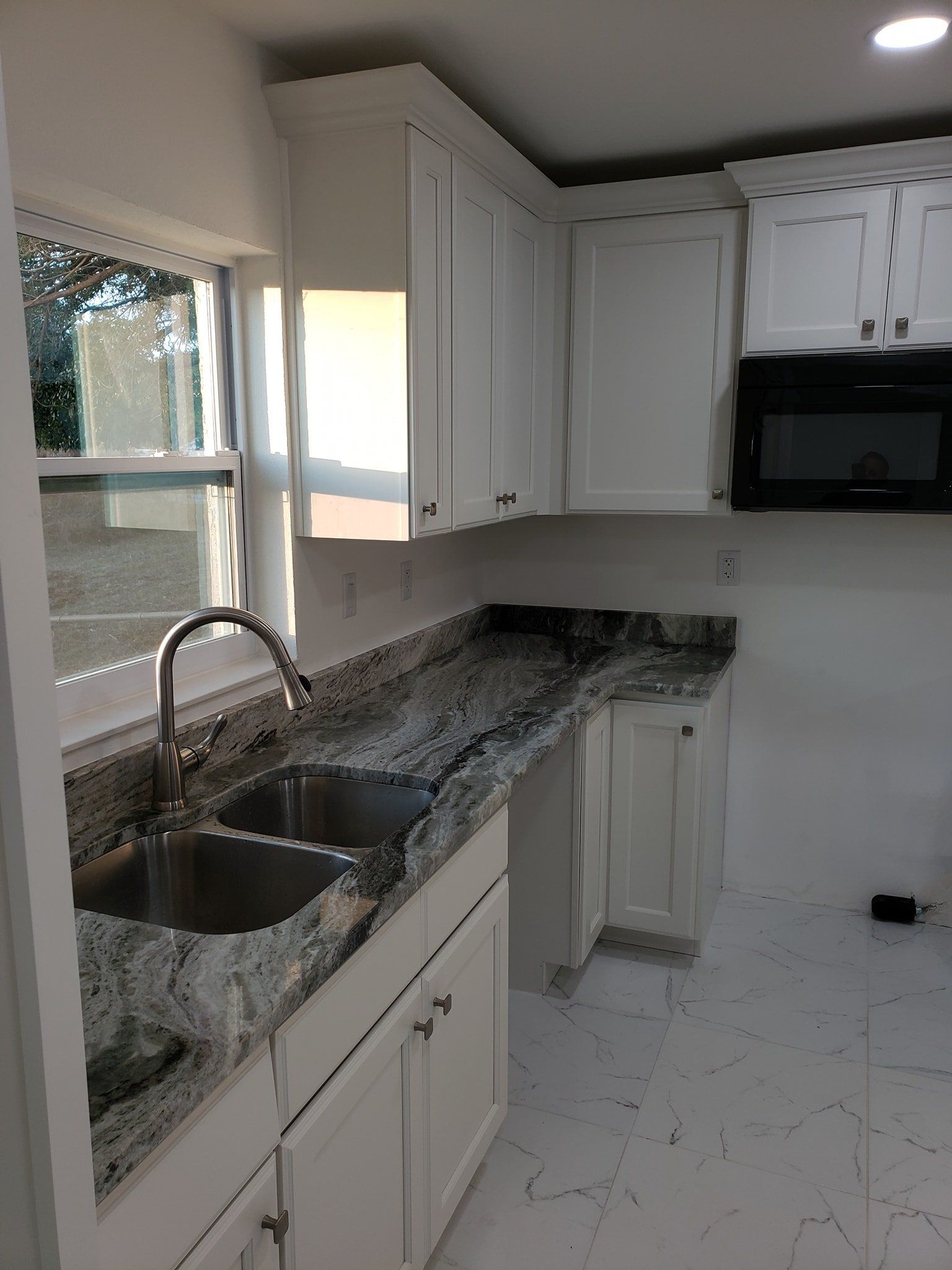 A modern kitchen featuring white cabinets, granite countertops, a double-basin sink, and a black microwave.
