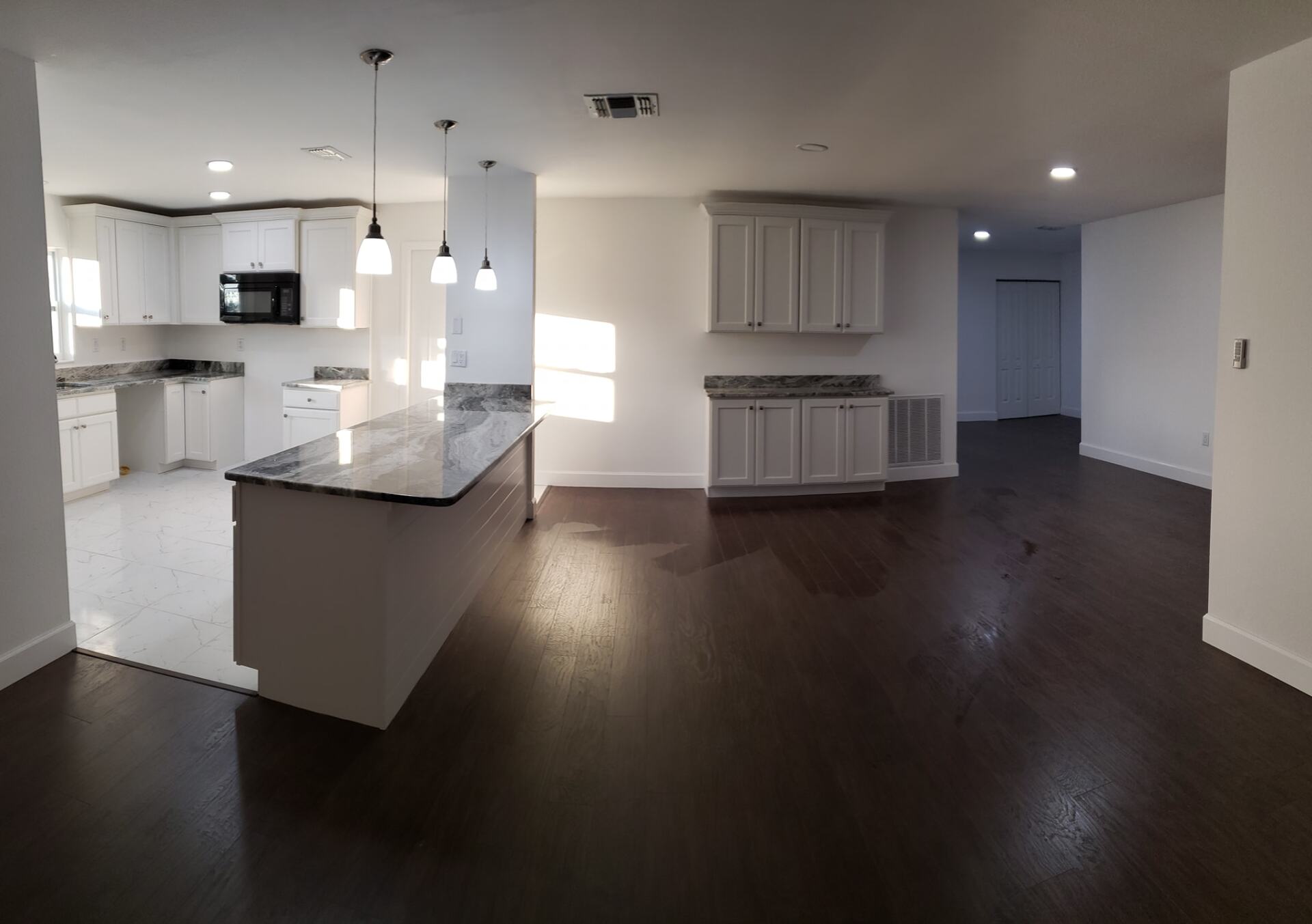A modern, open-concept kitchen featuring a large granite island, white cabinetry, and dark hardwood floors.