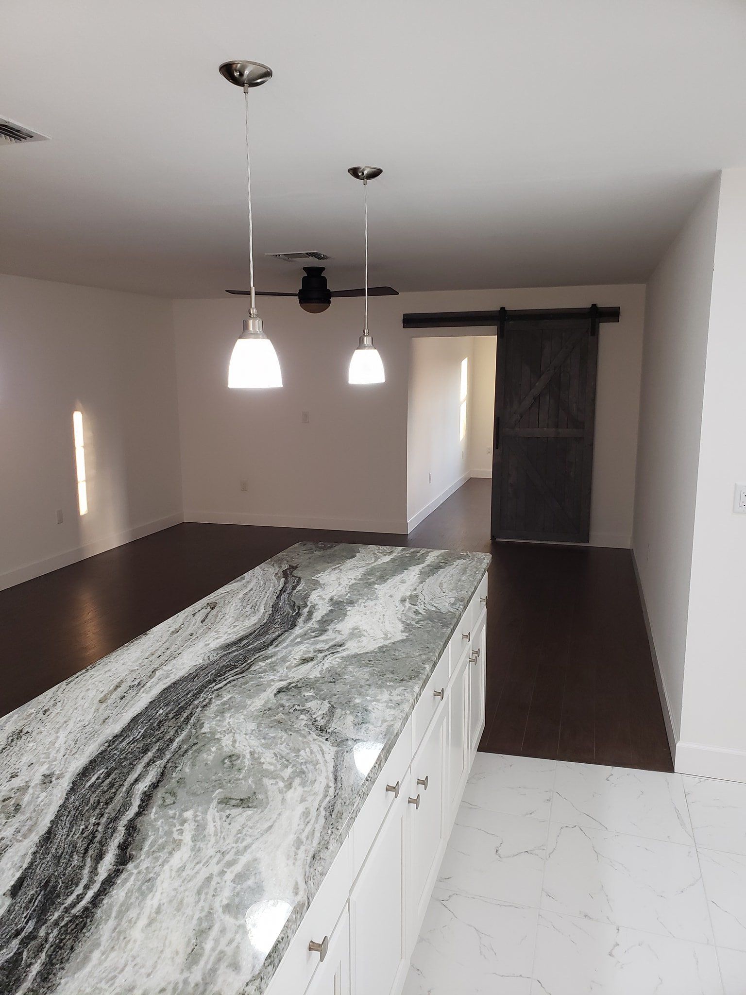 A modern kitchen island with a white and black marble countertop, two pendant lights, white cabinets, and dark flooring.