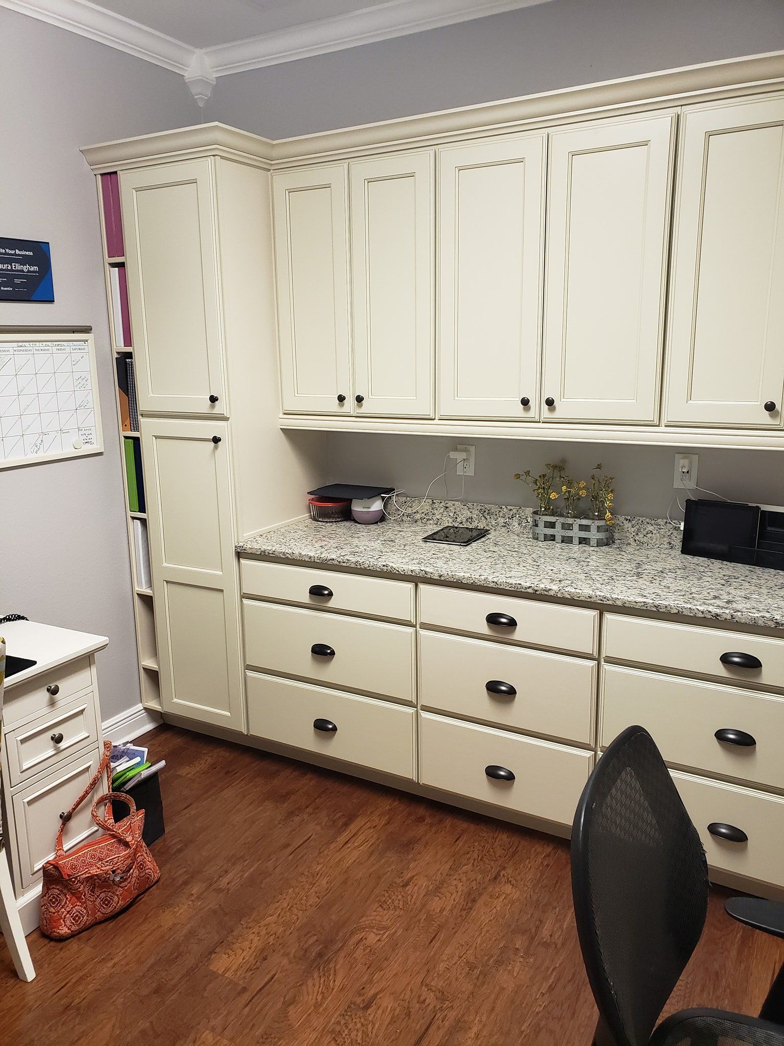 Cream-colored office cabinets with granite countertops and dark hardware arranged along a wall on a hardwood floor.