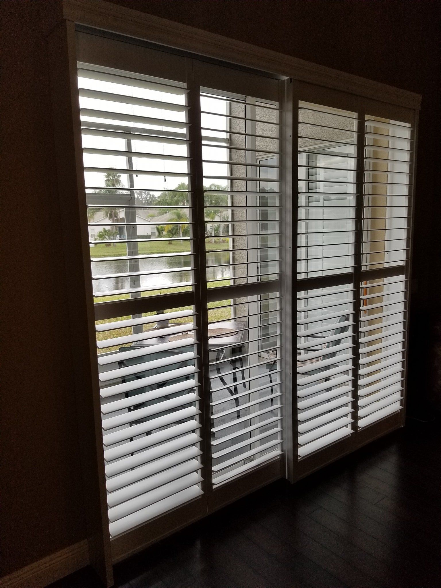 White plantation shutters installed on a large sliding glass door overlooking a patio and backyard lake.