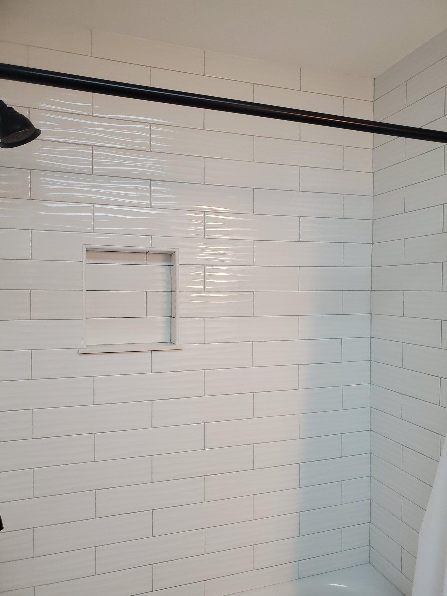 A shower wall with white, rectangular subway tiles in a running bond pattern and a square inset storage niche.