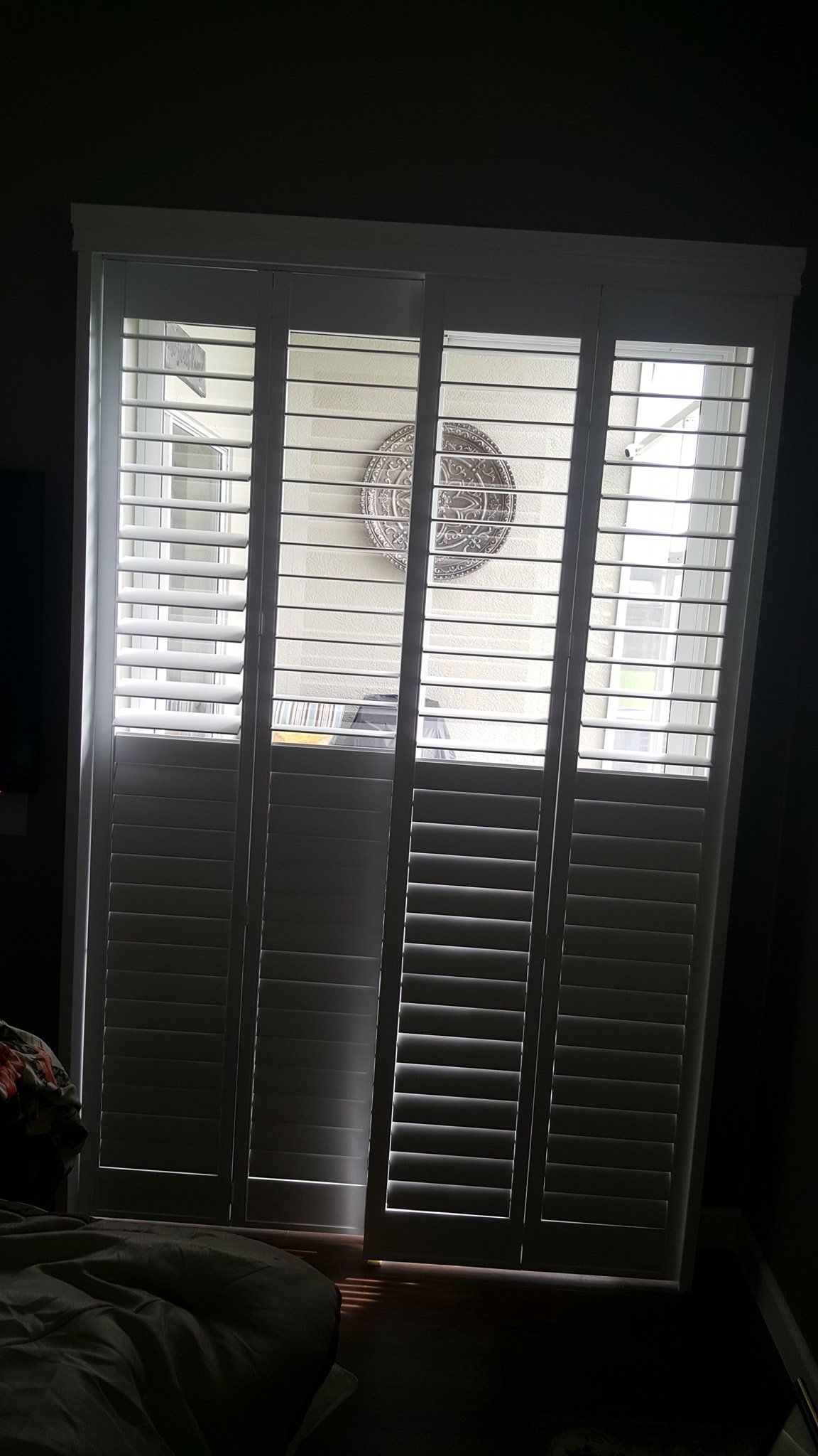 White louvered plantation shutters partially closed over a window, allowing light to shine through the horizontal slats.