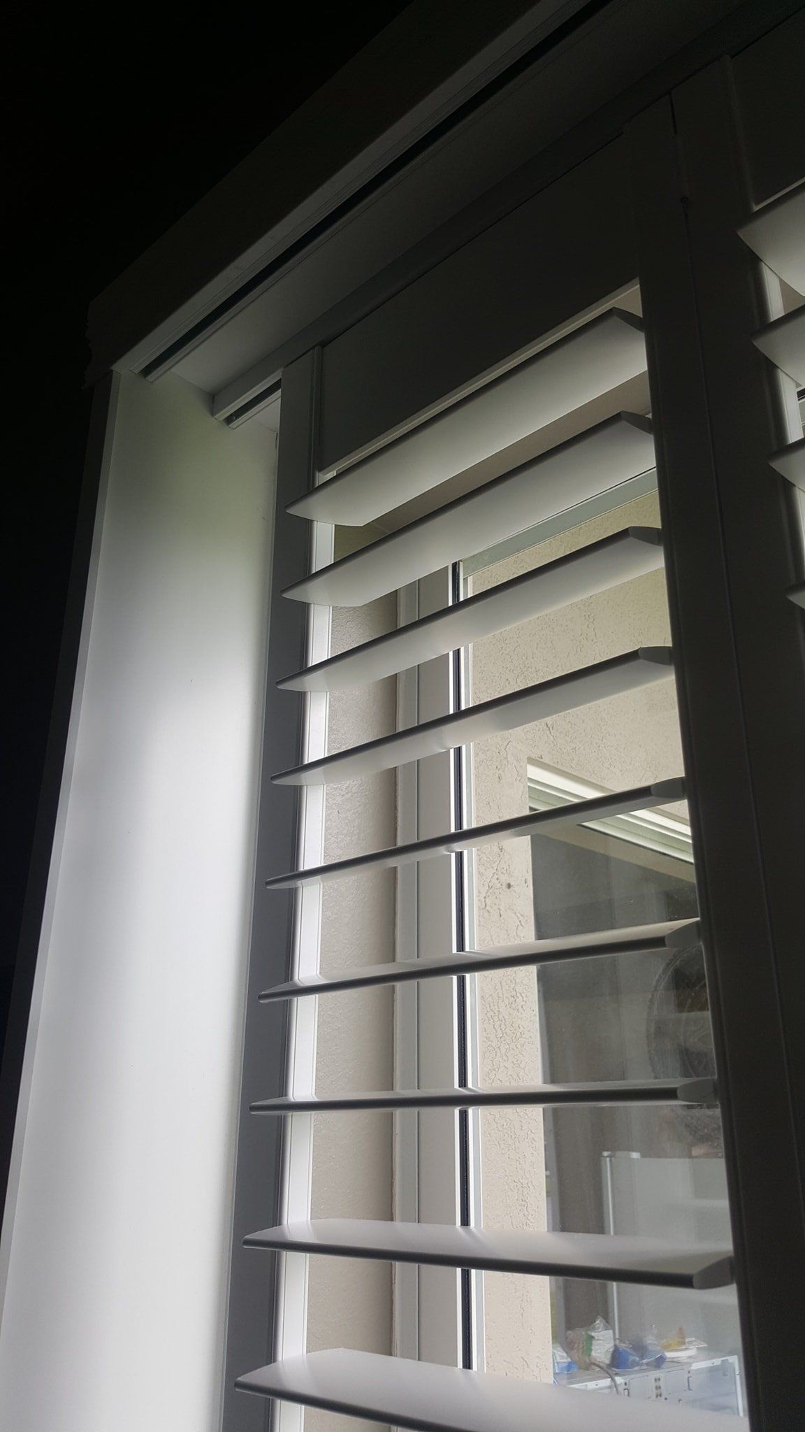 White interior shutters installed over a window, angled to allow light into a room at night.
