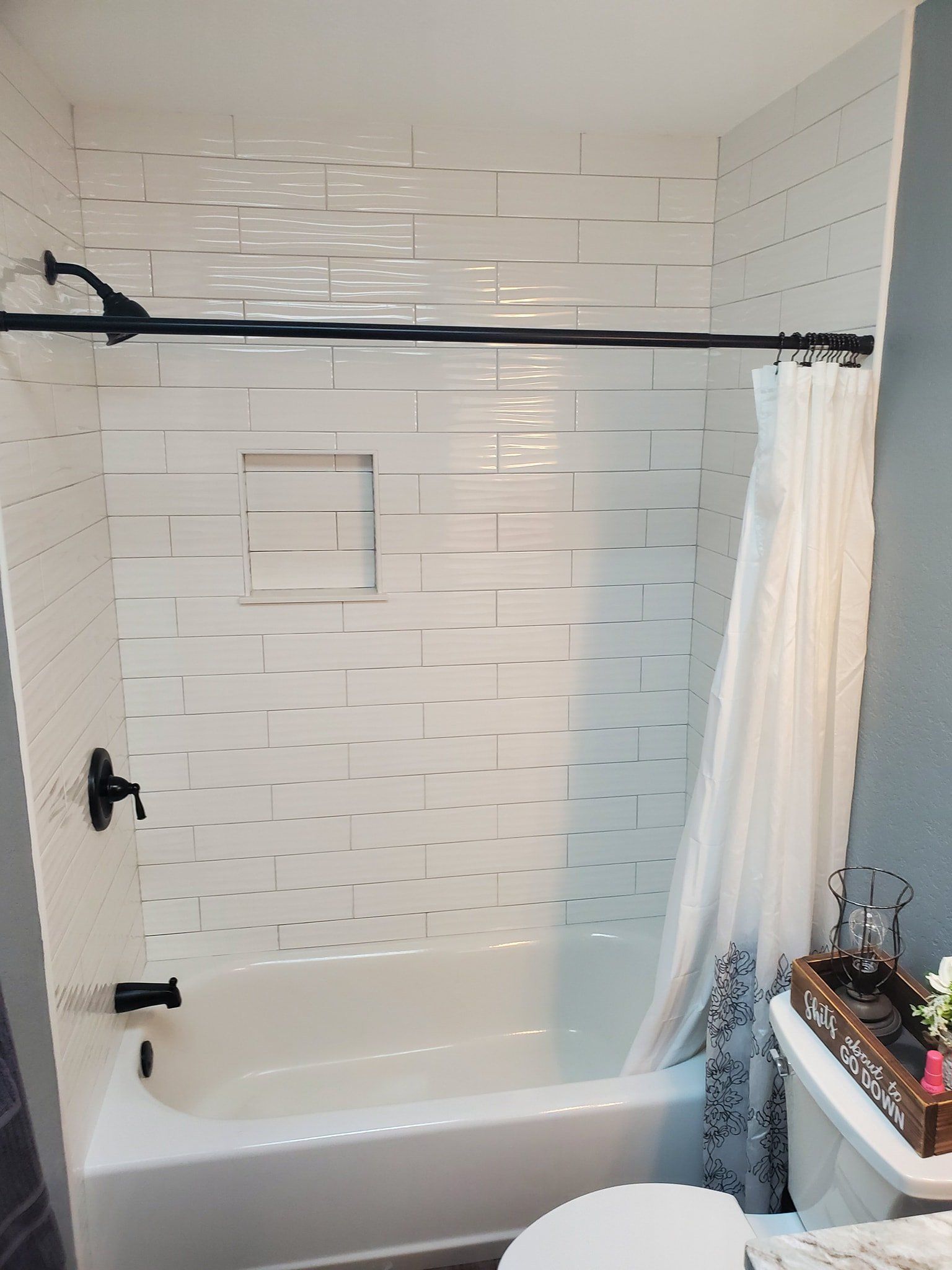A white bathtub and shower surround with white rectangular tiles, a black shower fixture, and a white curtain.