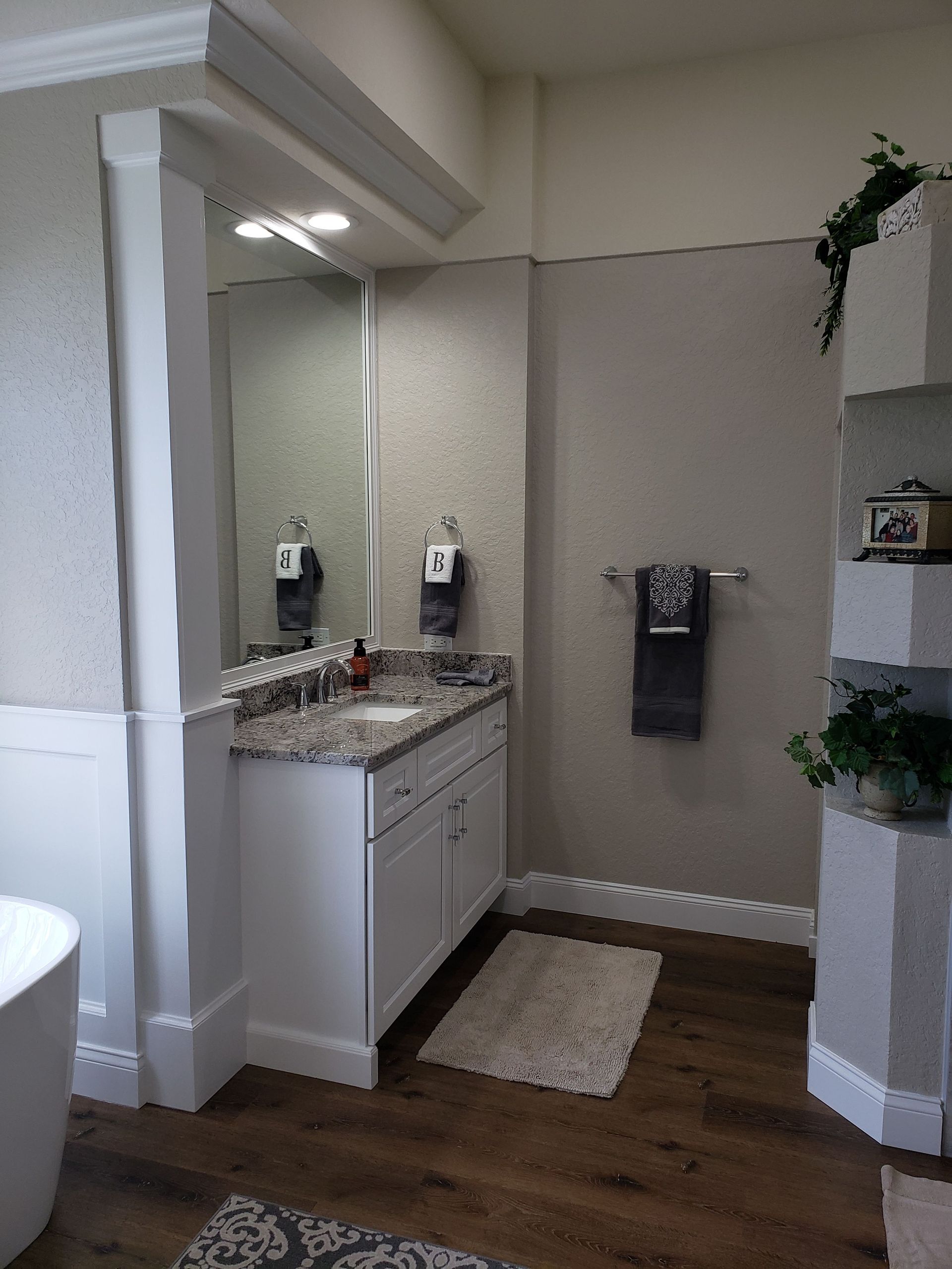 A modern bathroom features a white vanity with a granite countertop, a mirror, and beige walls with white trim.