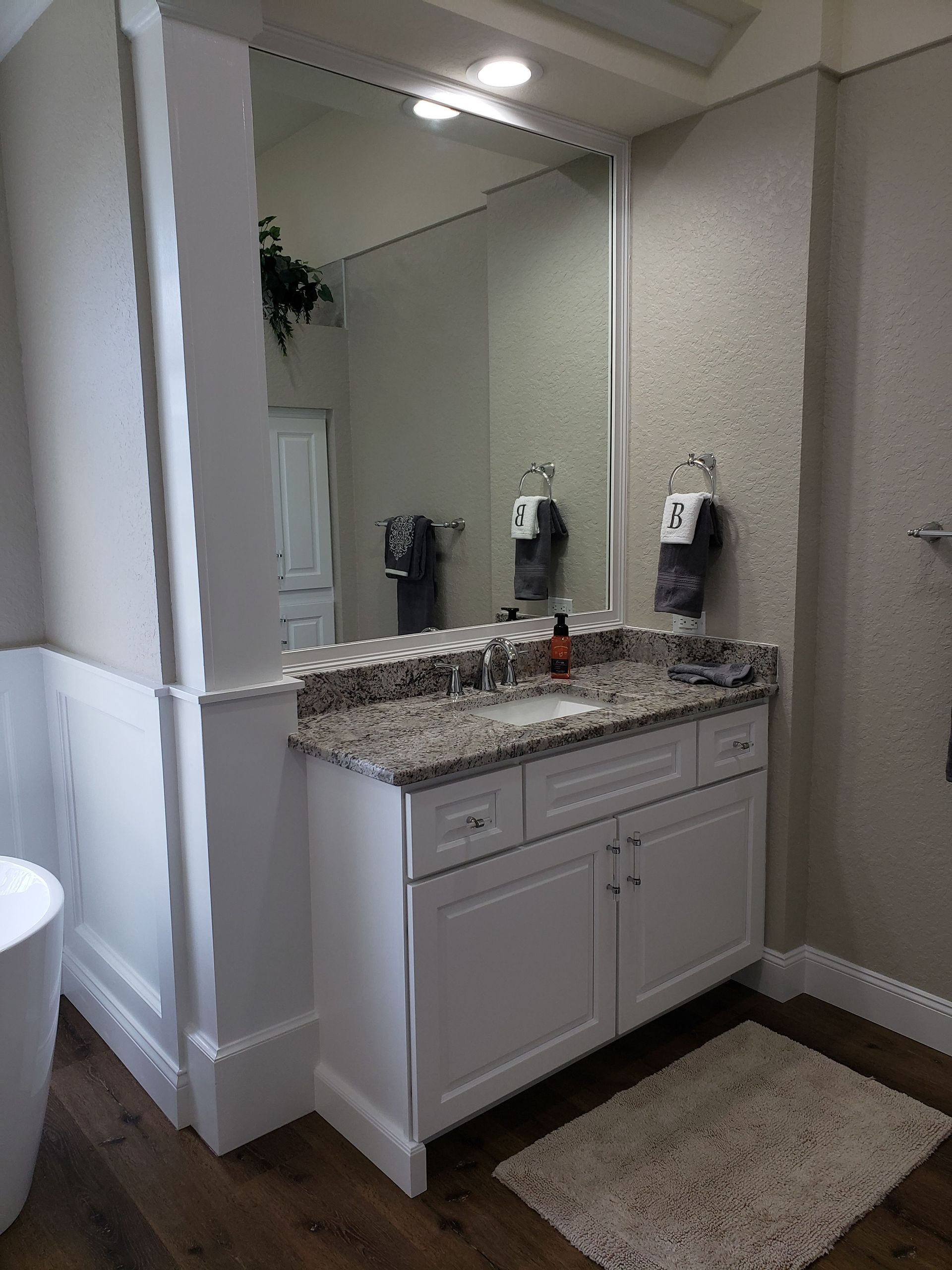 A white bathroom vanity with a speckled granite countertop, sink, and large mirror, set against textured beige walls.