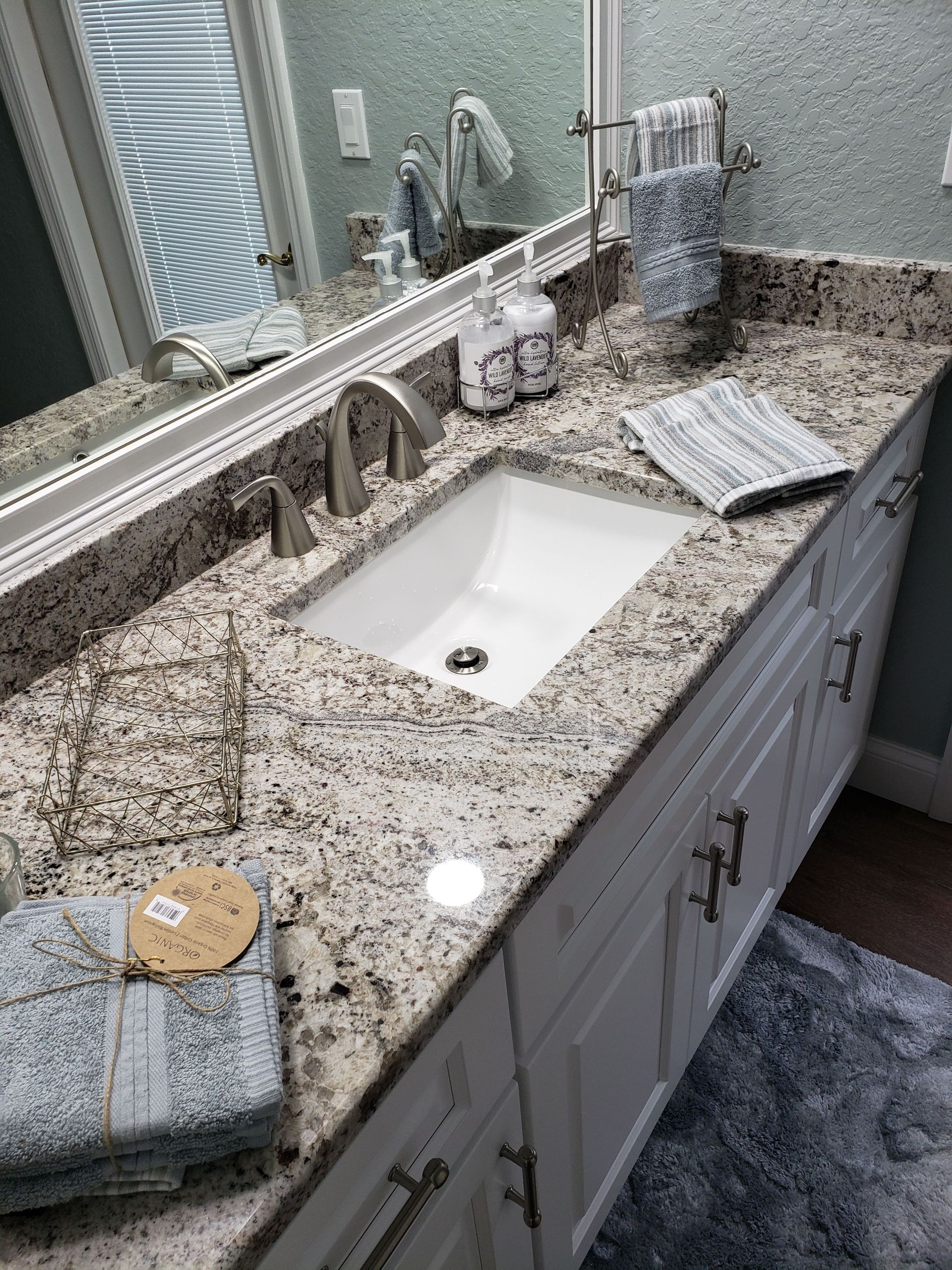 A bathroom vanity with a speckled granite countertop, white sink, faucet, and cabinet, with towels and accessories.