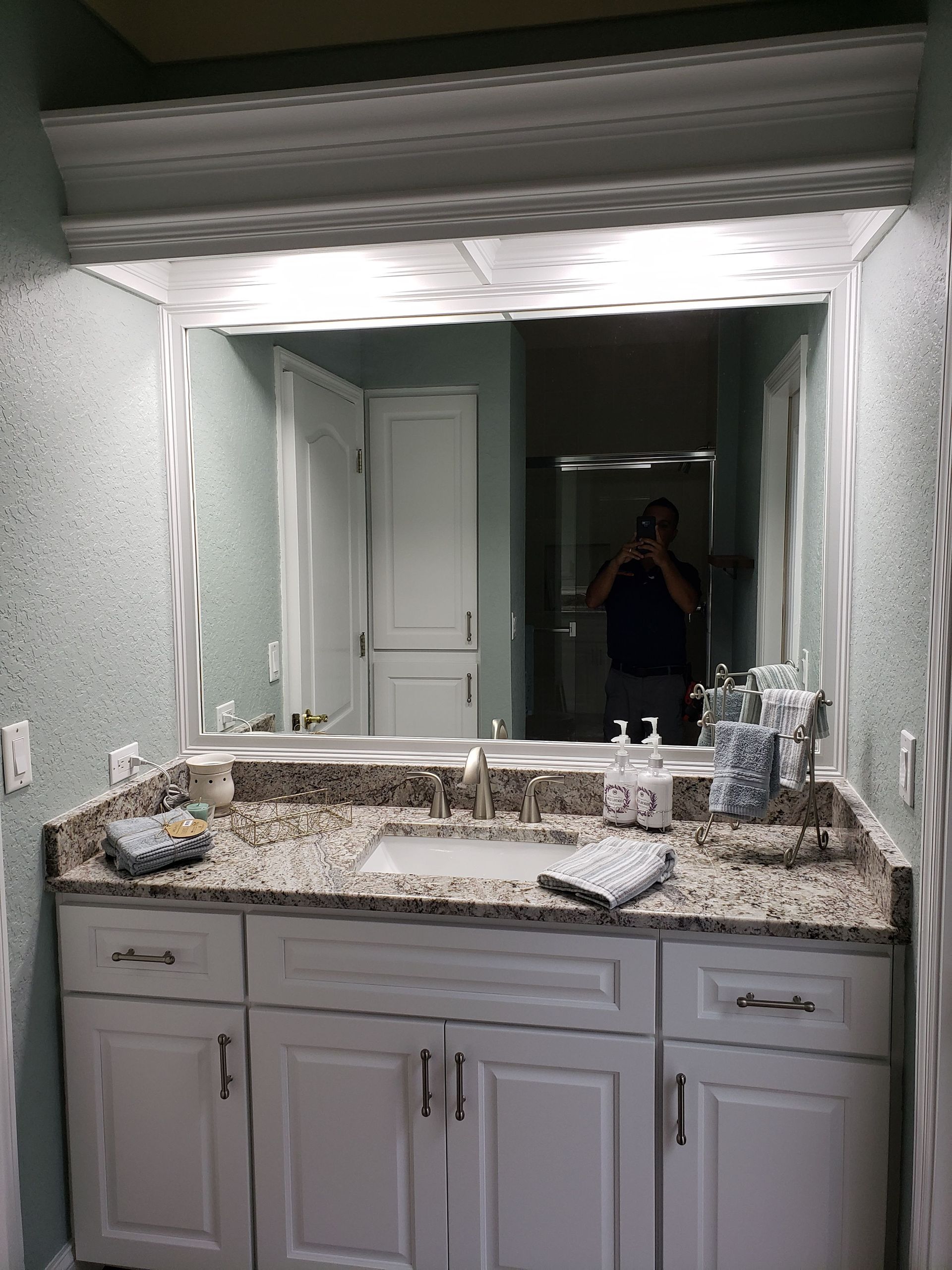 A bathroom vanity with a white cabinet, granite countertop, rectangular sink, and a large mirror with crown molding above.