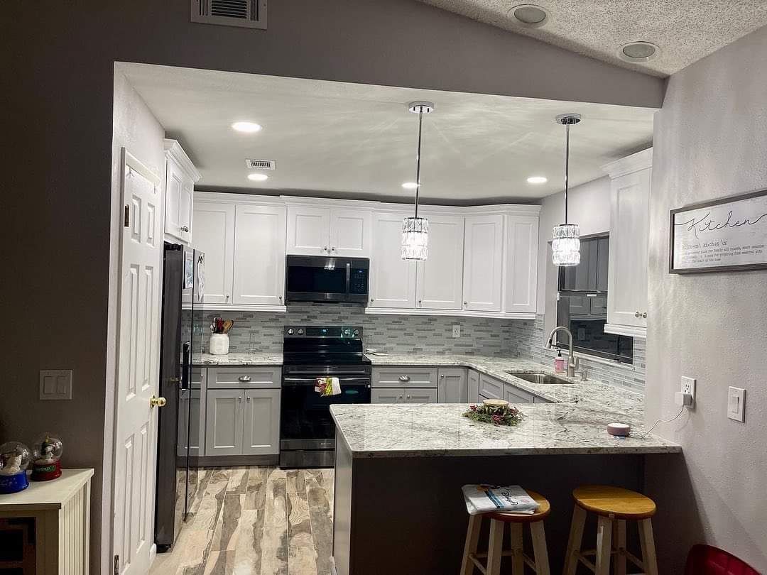 A kitchen with white cabinets, dark countertops, a black stove and microwave, and a peninsula with two wooden stools.