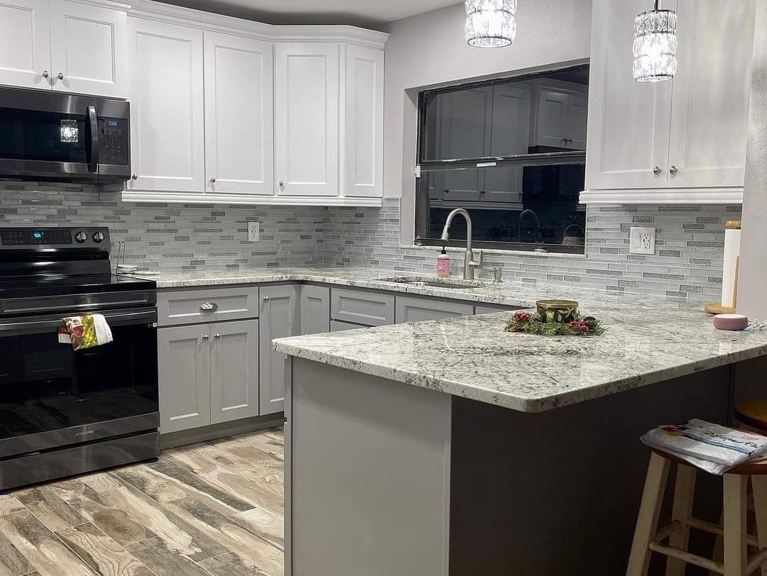 Modern kitchen featuring white cabinets, granite countertops, a black stove, tiled backsplash, and wooden flooring.