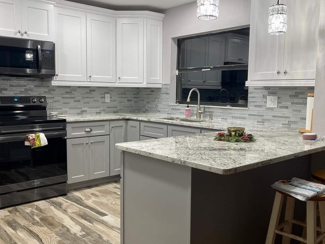 Modern kitchen with white upper cabinets, gray base cabinets, speckled granite countertops, and light wood-look flooring.