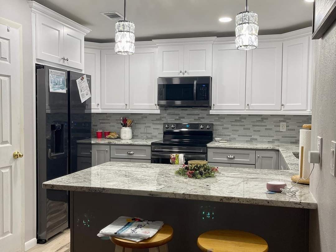 A modern kitchen with white cabinets, light gray lower cabinets, granite countertops, a black refrigerator, and an island.