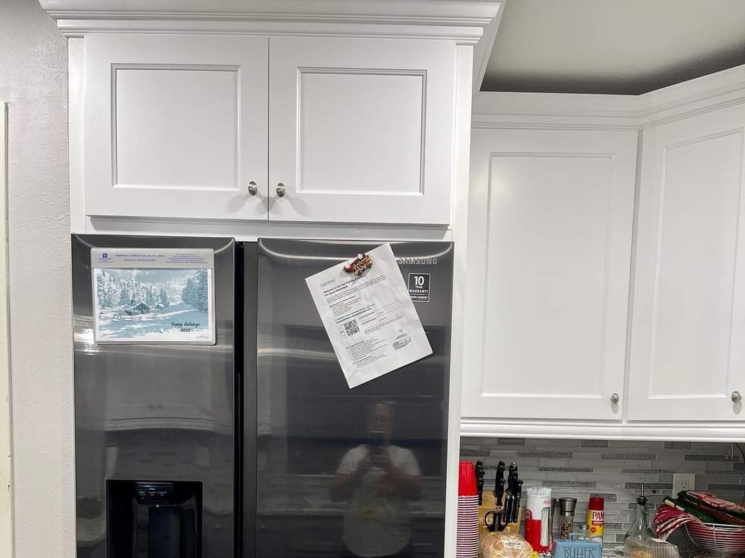 A stainless steel refrigerator with a paper pinned to the door, positioned beneath white kitchen cabinets.
