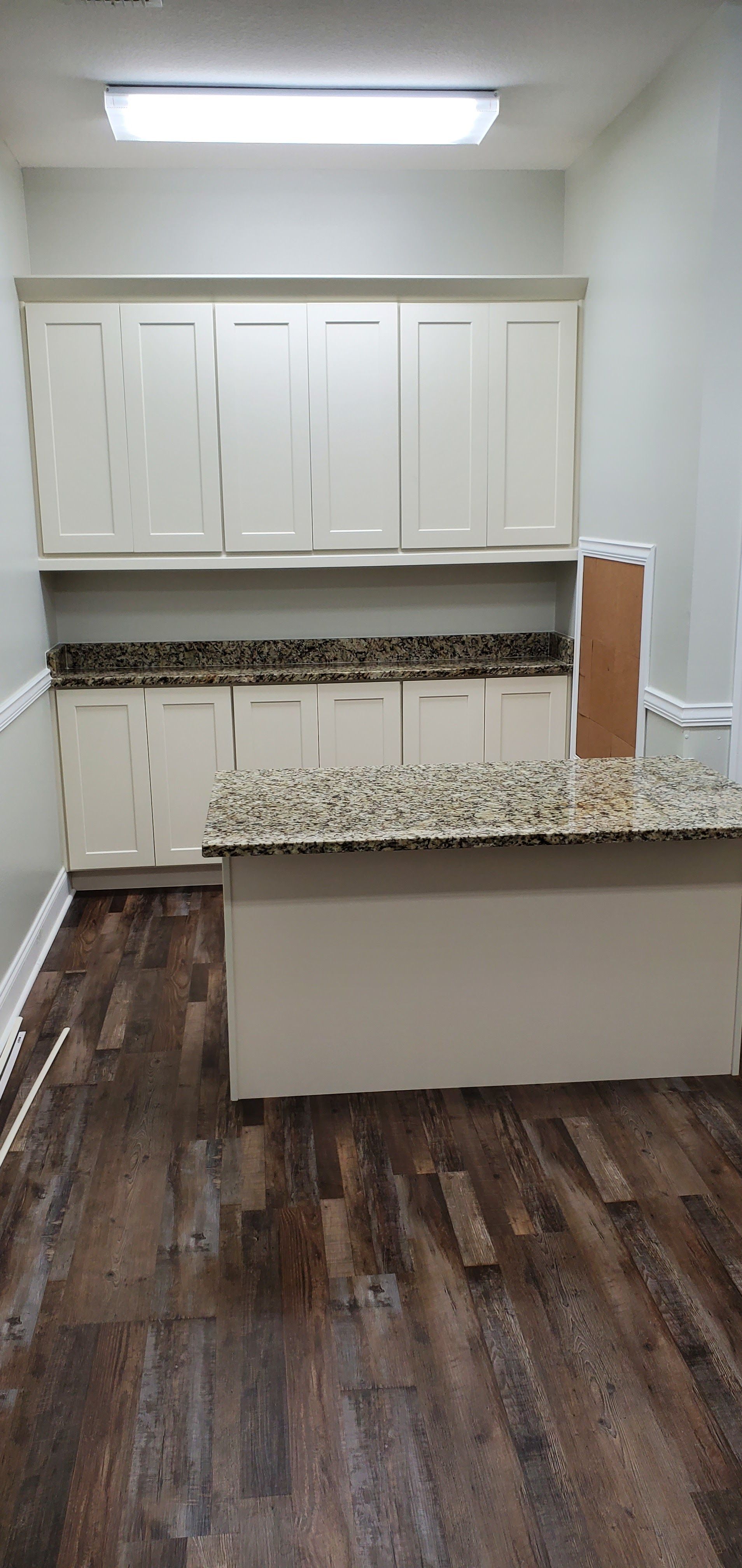 A kitchen with light-colored cabinets, granite countertops, an island, and dark wood-look flooring.