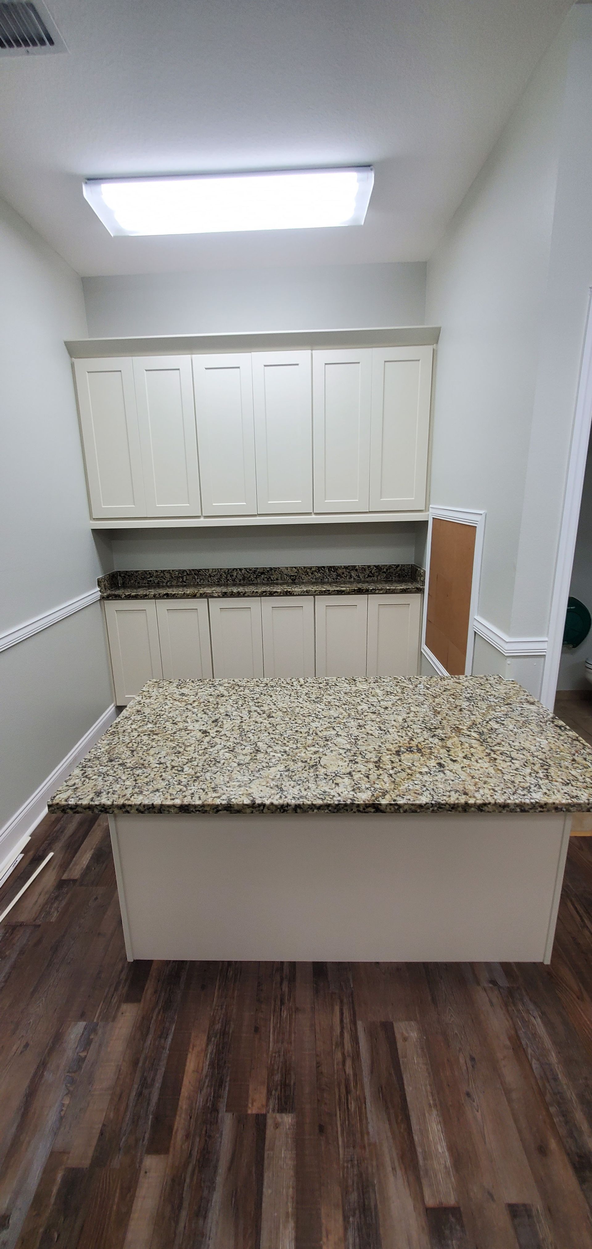 A kitchen area with a central island featuring tan granite countertops and white cabinets against a gray wall.