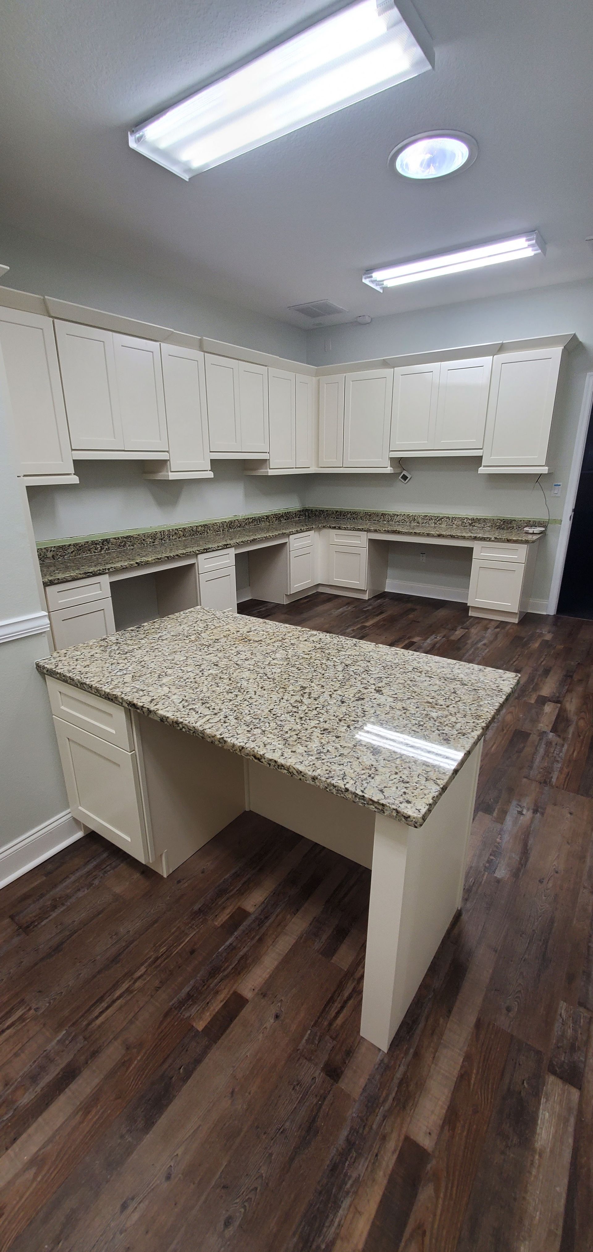 A modern office space features off-white cabinetry, speckled granite countertops, and dark hardwood flooring.