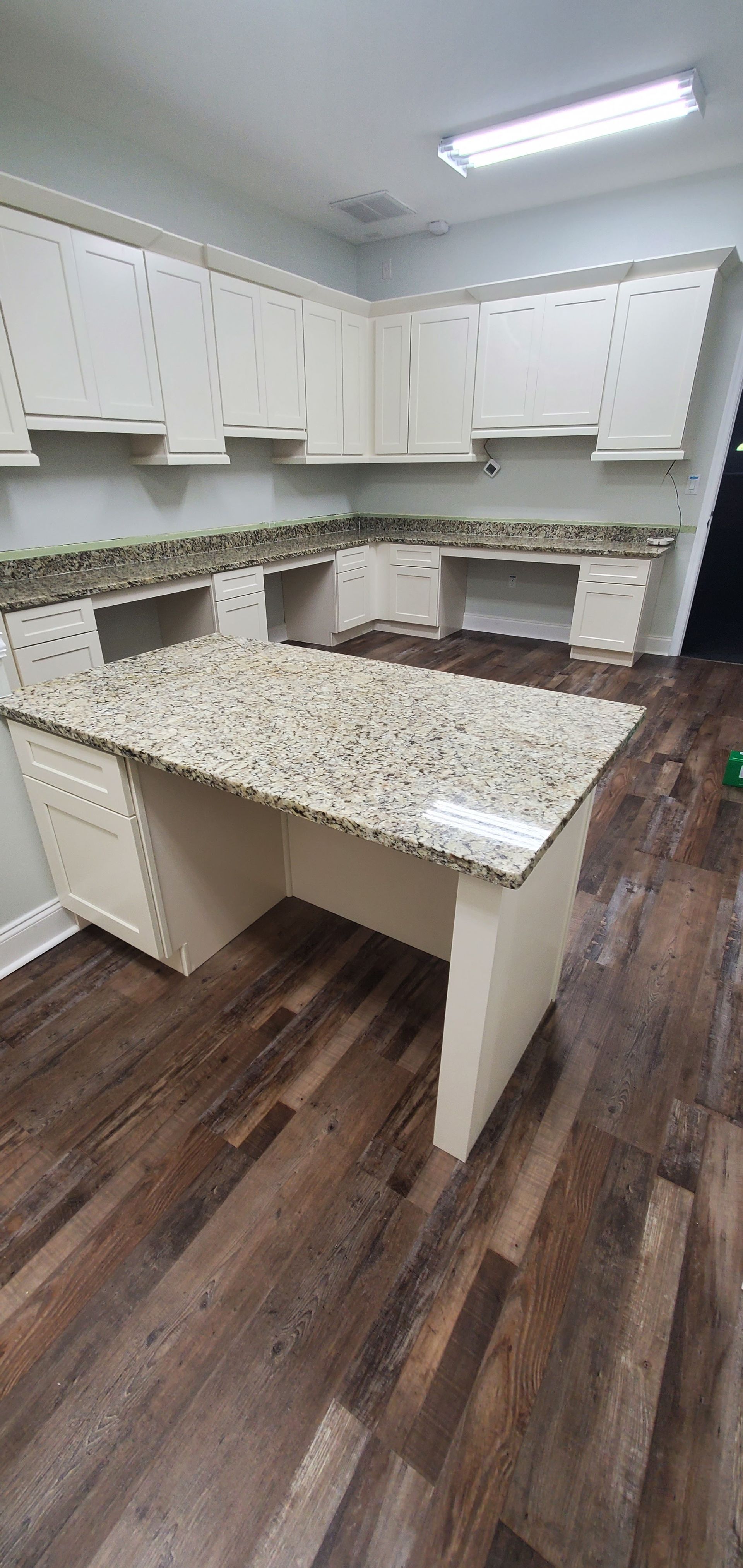 An L-shaped workspace with cream-colored cabinets, speckled granite countertops, and wood-grain flooring.