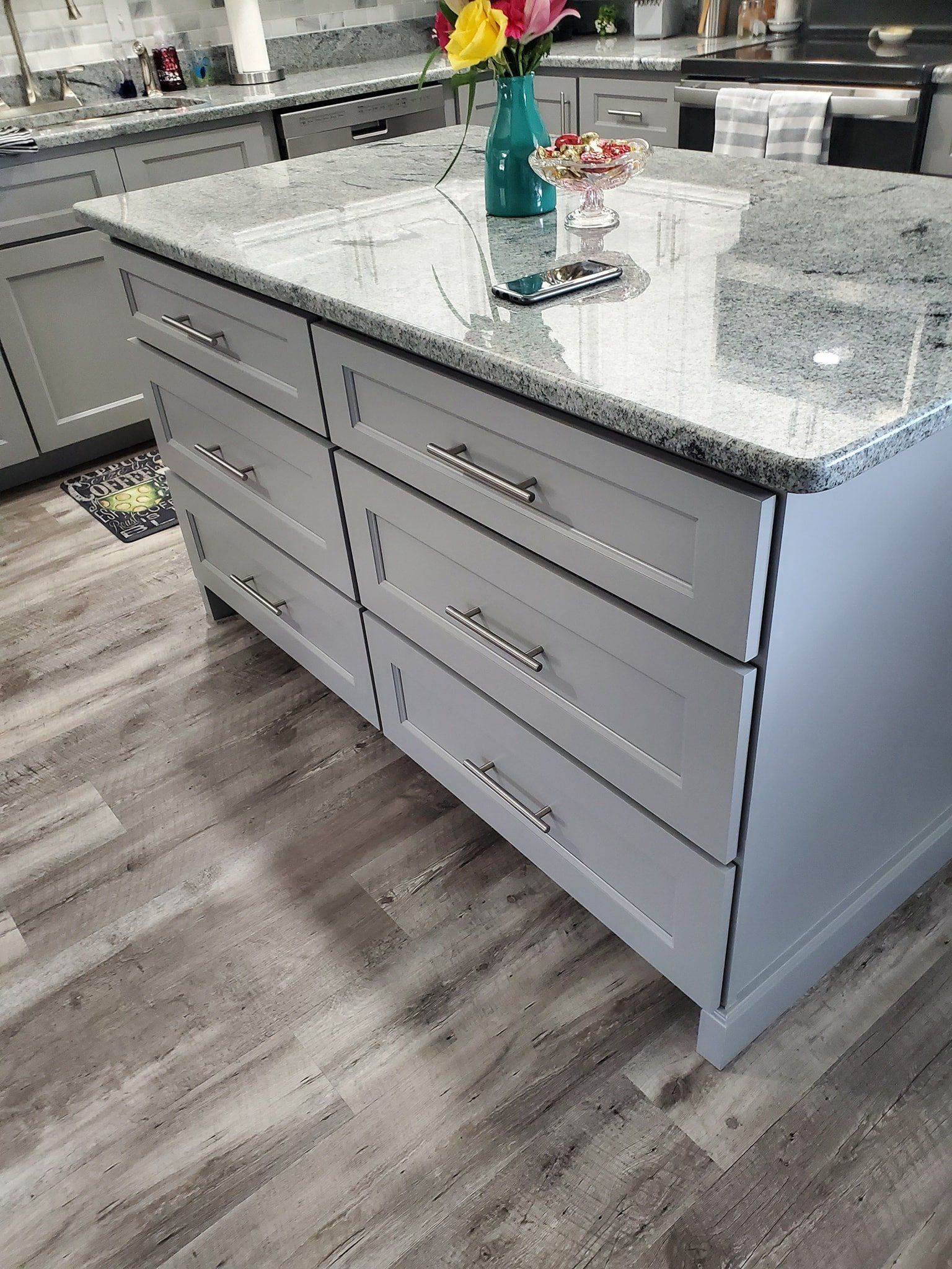 A kitchen island with light gray drawers and a speckled granite countertop in a home kitchen.