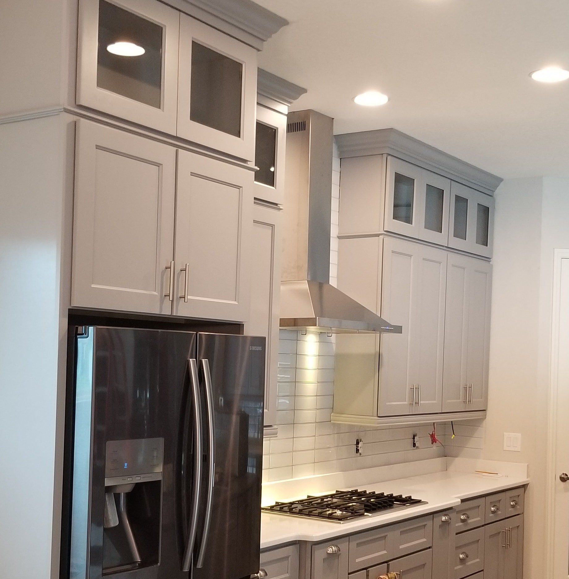 A modern kitchen featuring light gray cabinetry, glass-paneled upper cabinets, stainless steel appliances, and a range.