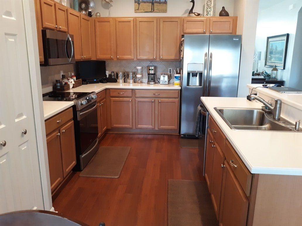 A U-shaped kitchen with light wood cabinets, white countertops, stainless steel appliances, and dark hardwood floors.