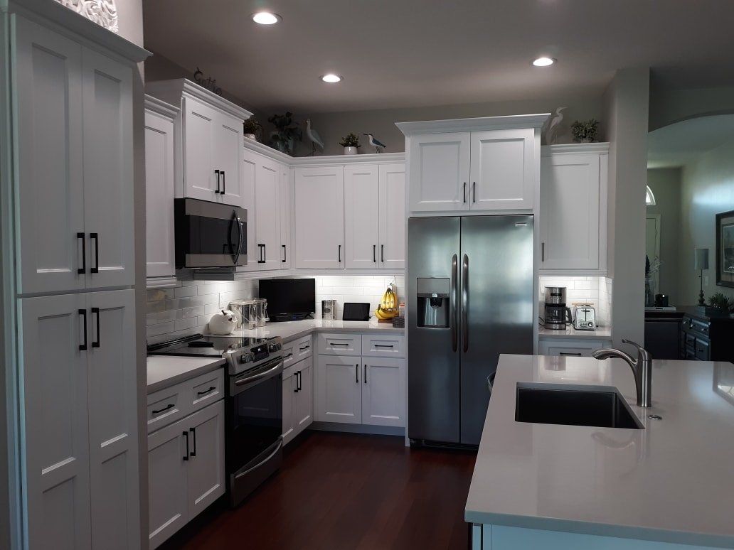 Modern kitchen featuring white cabinets, stainless steel appliances, a dark wooden floor, and a white kitchen island.