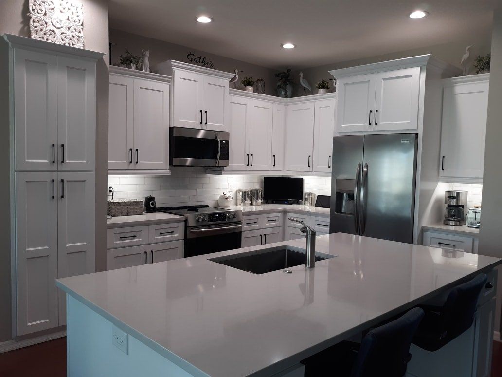 A modern kitchen features white cabinets, stainless steel appliances, and a large white quartz island with a sink.