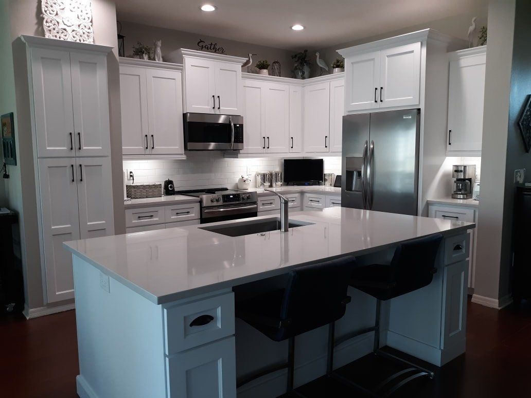 A modern kitchen featuring white cabinets, stainless steel appliances, a large central island, and dark wood flooring.