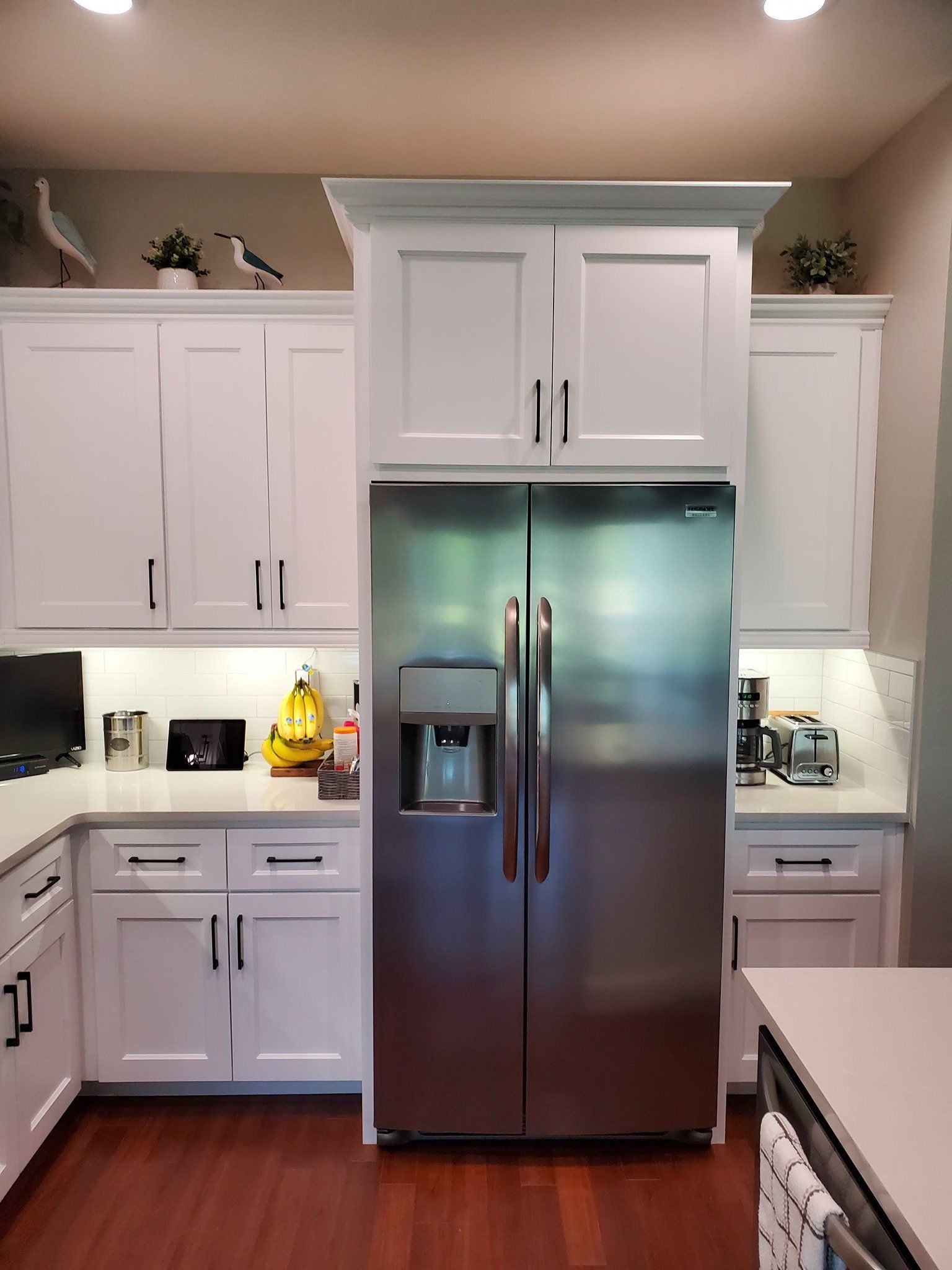 A kitchen featuring white cabinets, a stainless steel refrigerator, and wood flooring with decorative birds on display.