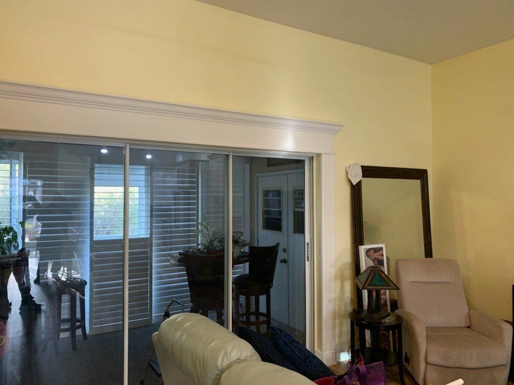 A living room with light yellow walls, a large sliding glass door with white trim, a tan armchair, and a floor mirror.