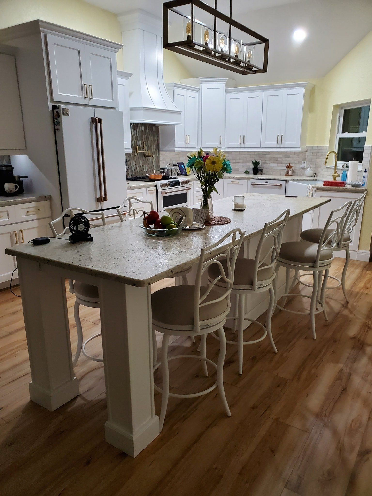 A kitchen featuring white cabinets, a large island with granite countertops, and bar seating on light wood floors.