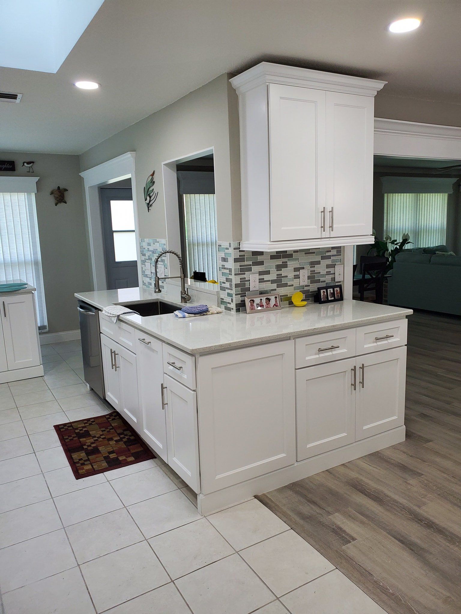A bright kitchen island with white cabinets, light quartz countertops, and a gray-and-white tile backsplash.