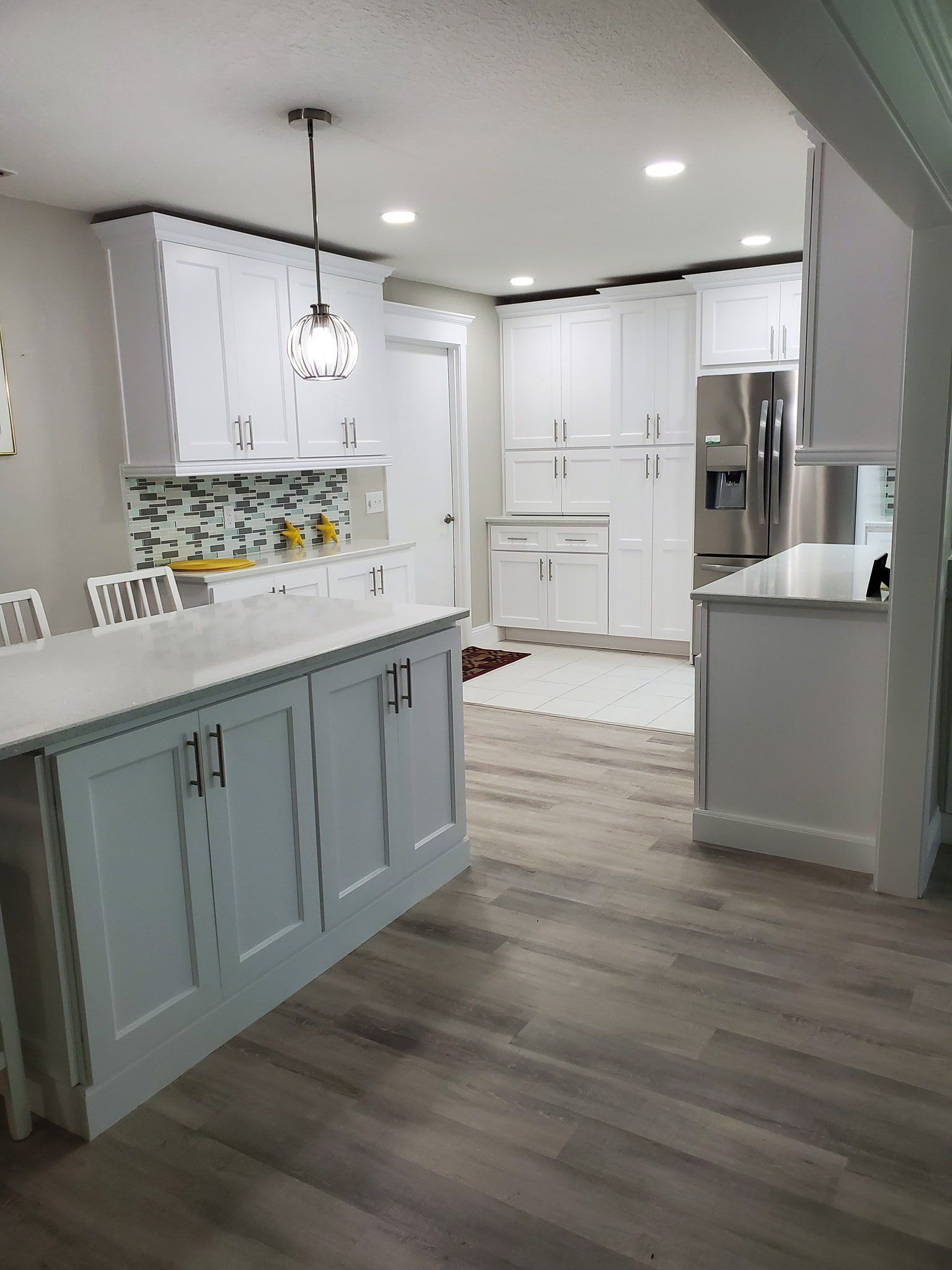 A modern kitchen with light gray cabinets, white countertops, stainless steel appliances, and wood-look flooring.