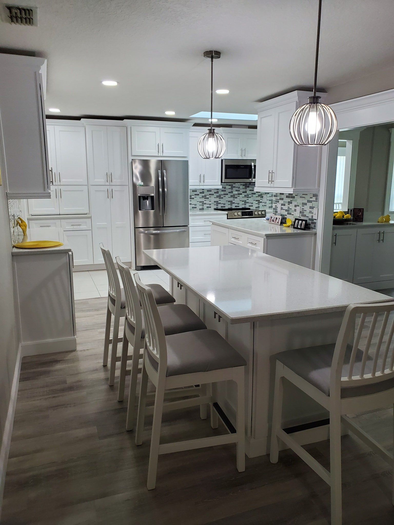 A modern kitchen featuring white cabinets, stainless steel appliances, an island with bar stools, and light wood flooring.