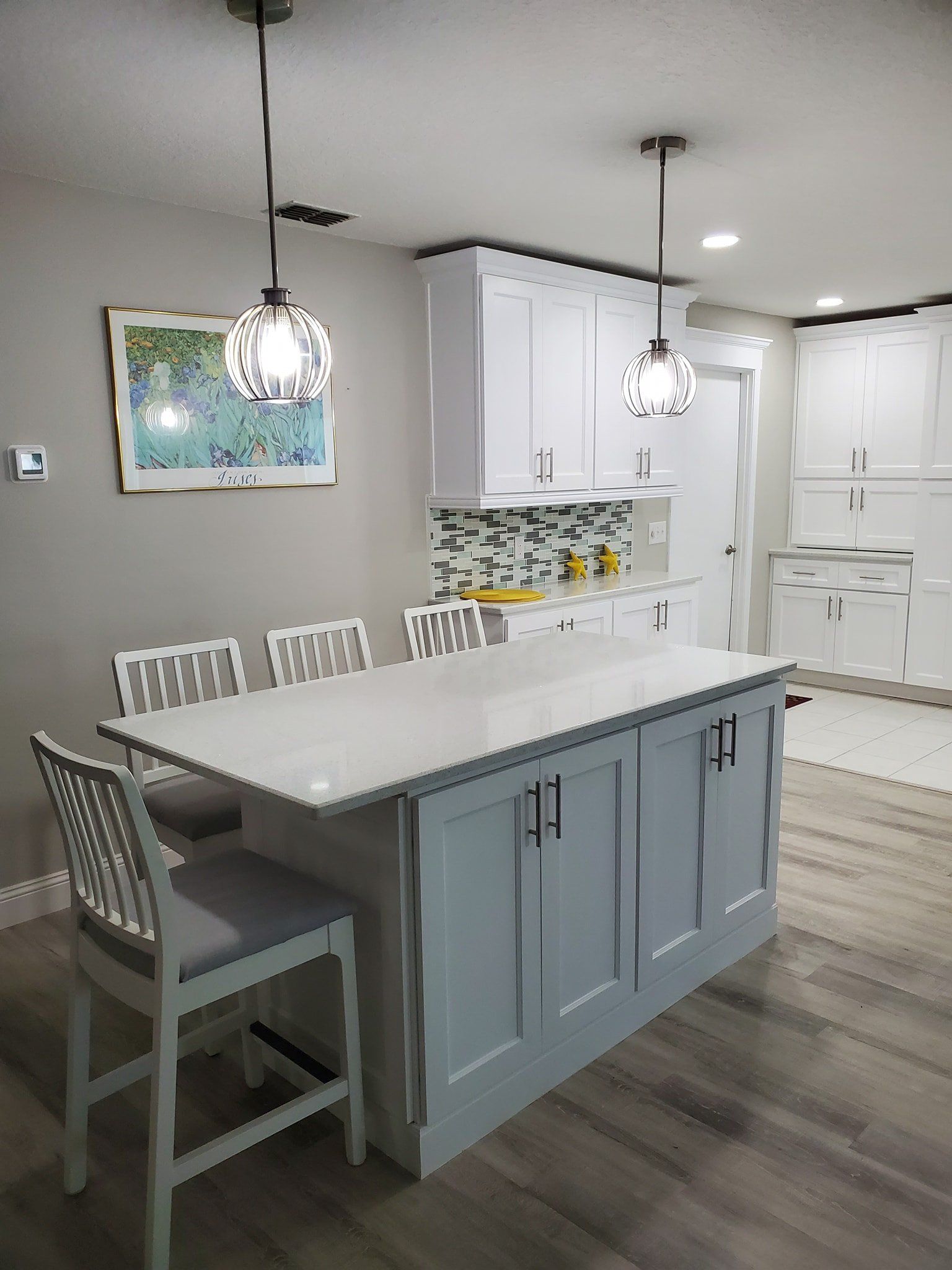A kitchen island with gray base cabinets and white countertop, accompanied by three gray-cushioned chairs.