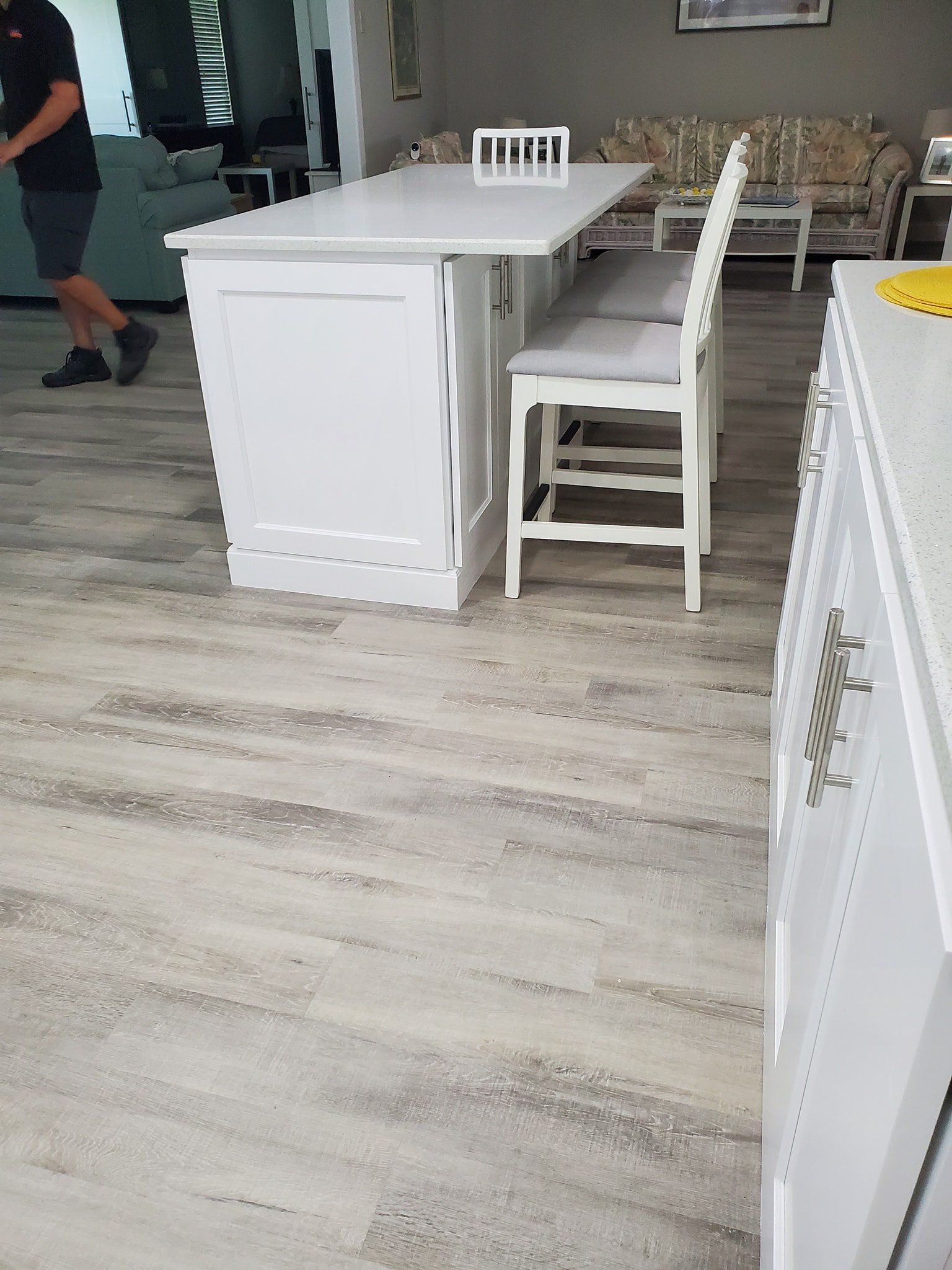 A modern kitchen with white cabinetry and a central island with high-backed chairs on a light-colored wood-look floor.
