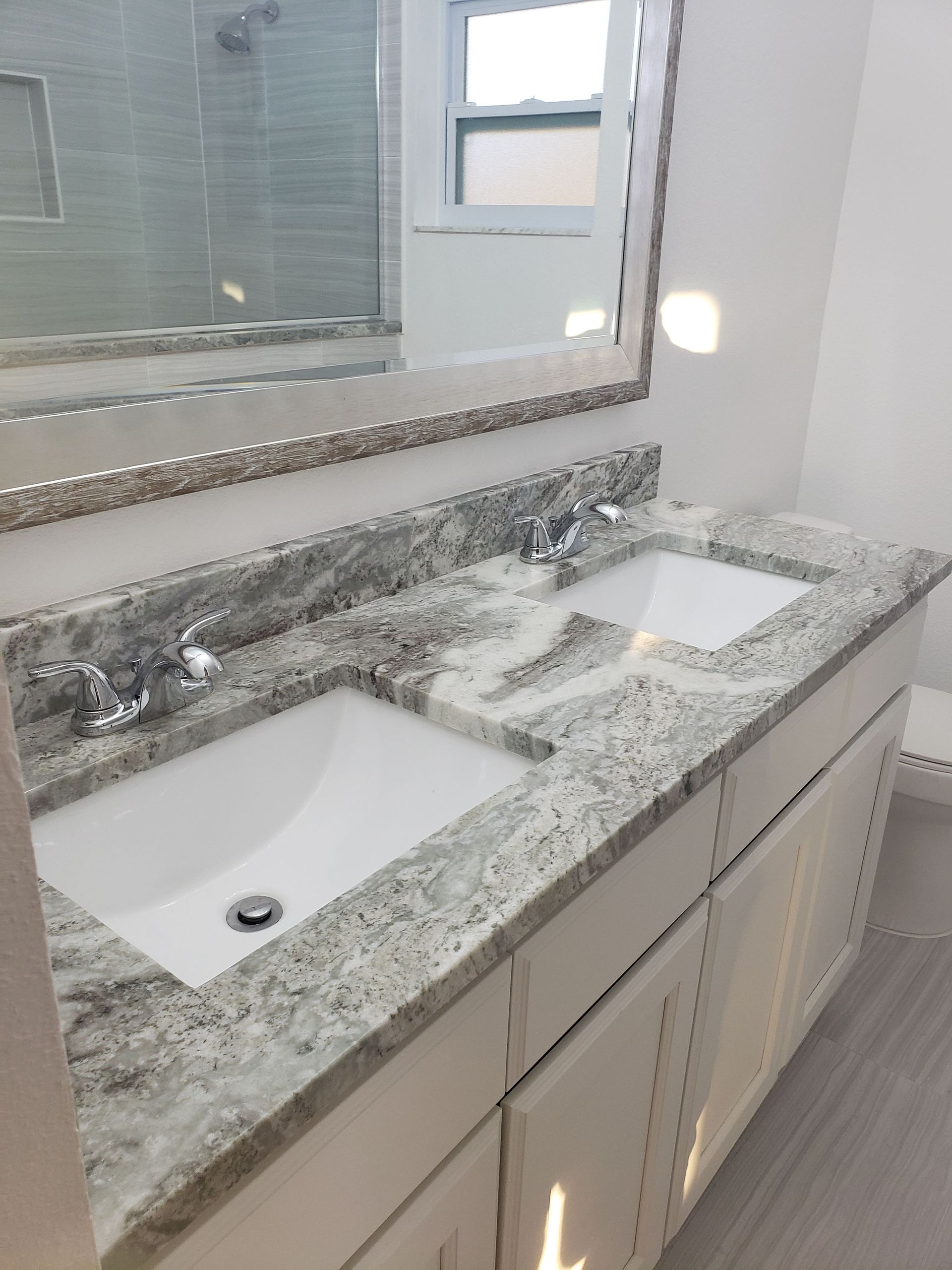 A double-sink bathroom vanity with a speckled granite countertop, white cabinets, and a framed mirror above.