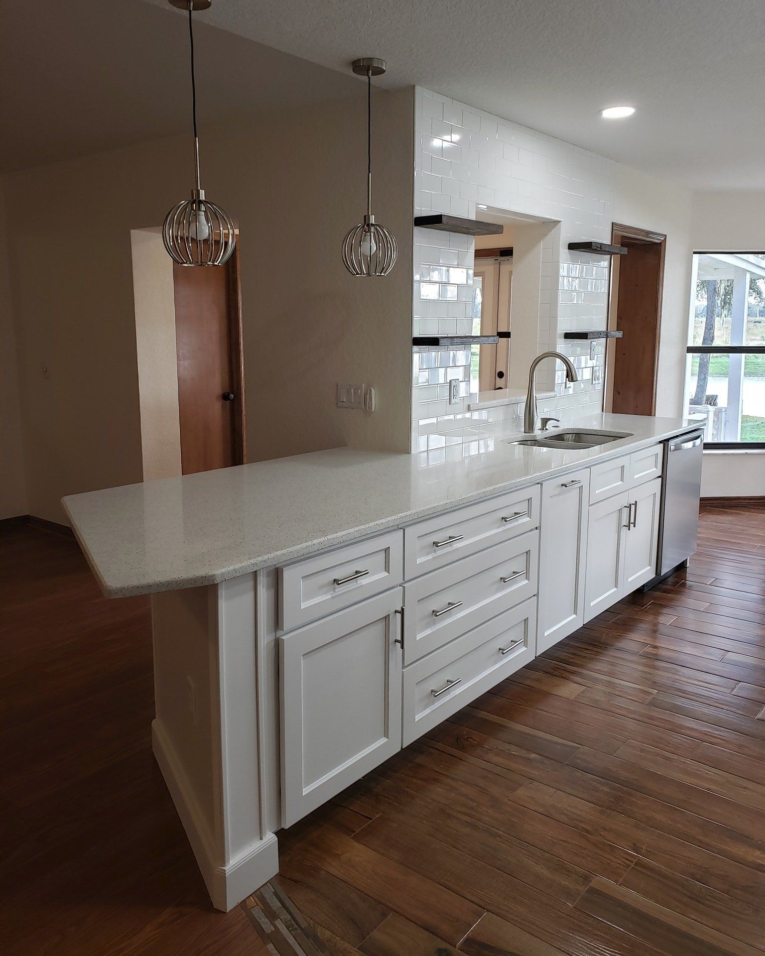 A modern kitchen island with white cabinets, a light-colored countertop, and two pendant lights on a wood floor.