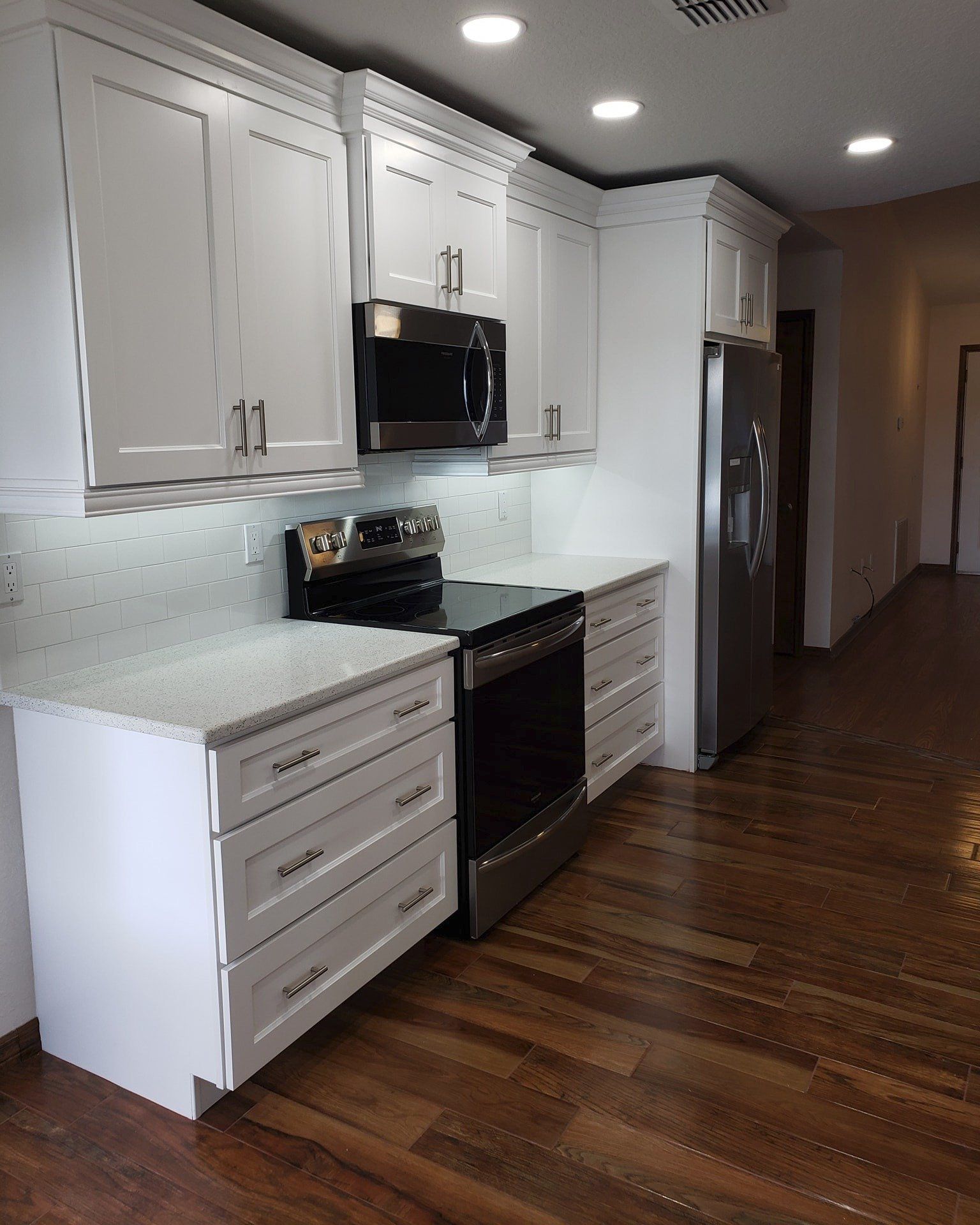 A modern kitchen featuring white cabinets, stainless steel appliances, speckled countertops, and wood flooring.
