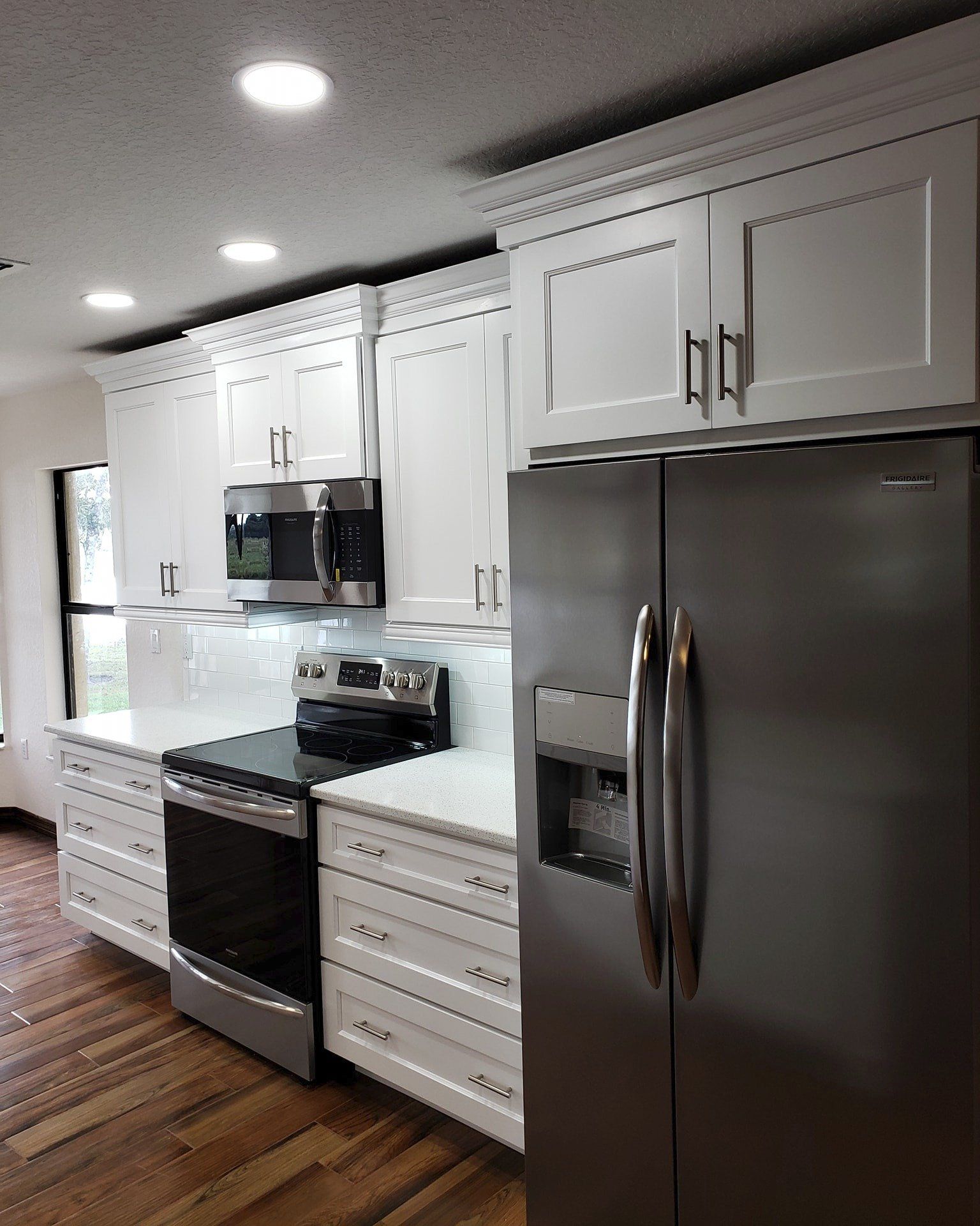 A modern kitchen featuring white cabinets, stainless steel appliances, a tiled backsplash, and dark wood flooring.