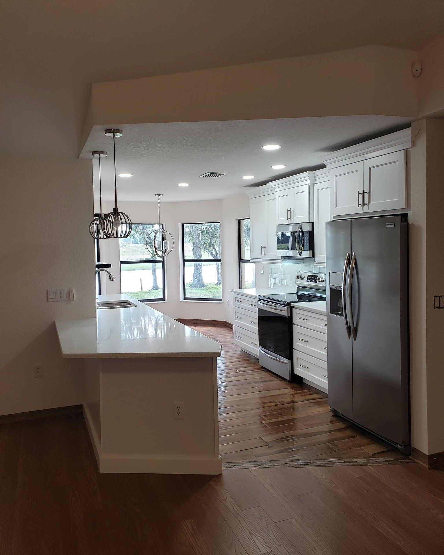 A modern kitchen with white cabinets, stainless steel appliances, a center island with pendant lights, and wood flooring.