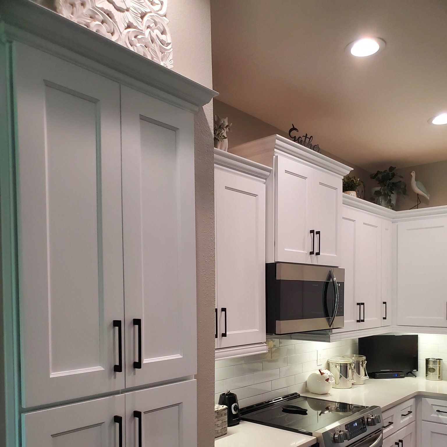 A modern kitchen featuring white shaker-style cabinets, dark hardware, and a stainless steel microwave above the stove.