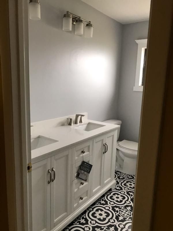 A bathroom featuring a white double-sink vanity, light gray walls, and black-and-white patterned floor tiles.