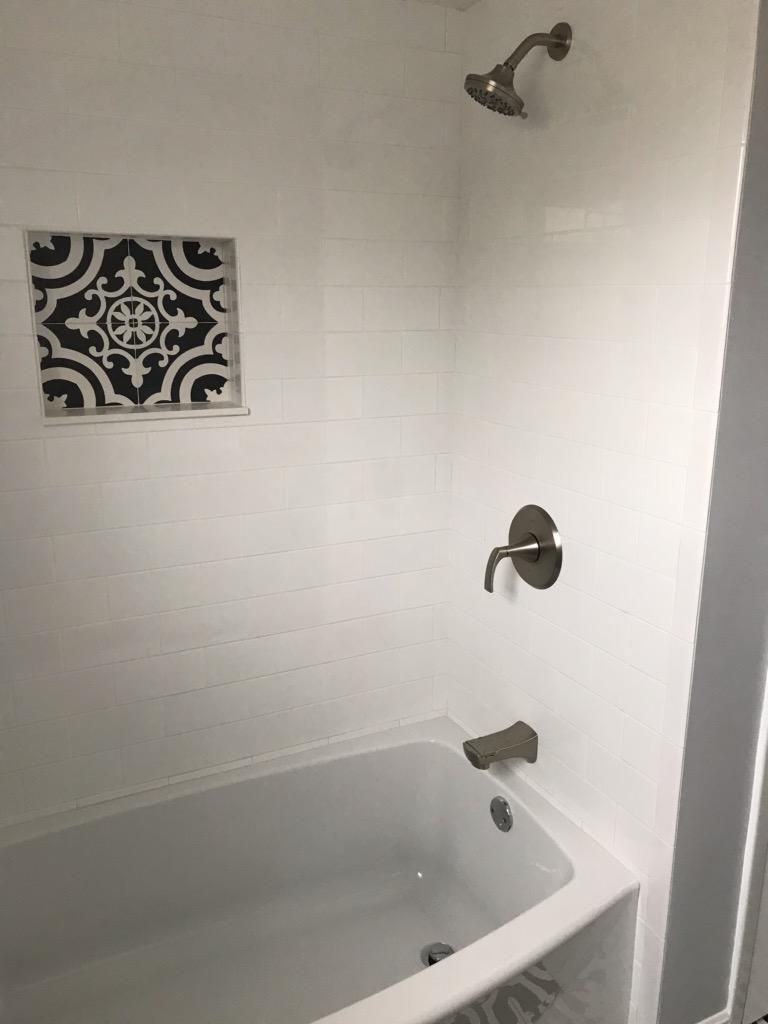 A white bathtub with a shower head and faucet featuring a decorative, patterned black and white tile wall niche.