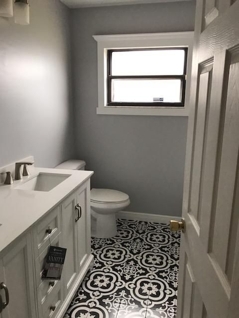 A bathroom with gray walls, white vanity, and black-and-white patterned tile flooring, seen through an open doorway.