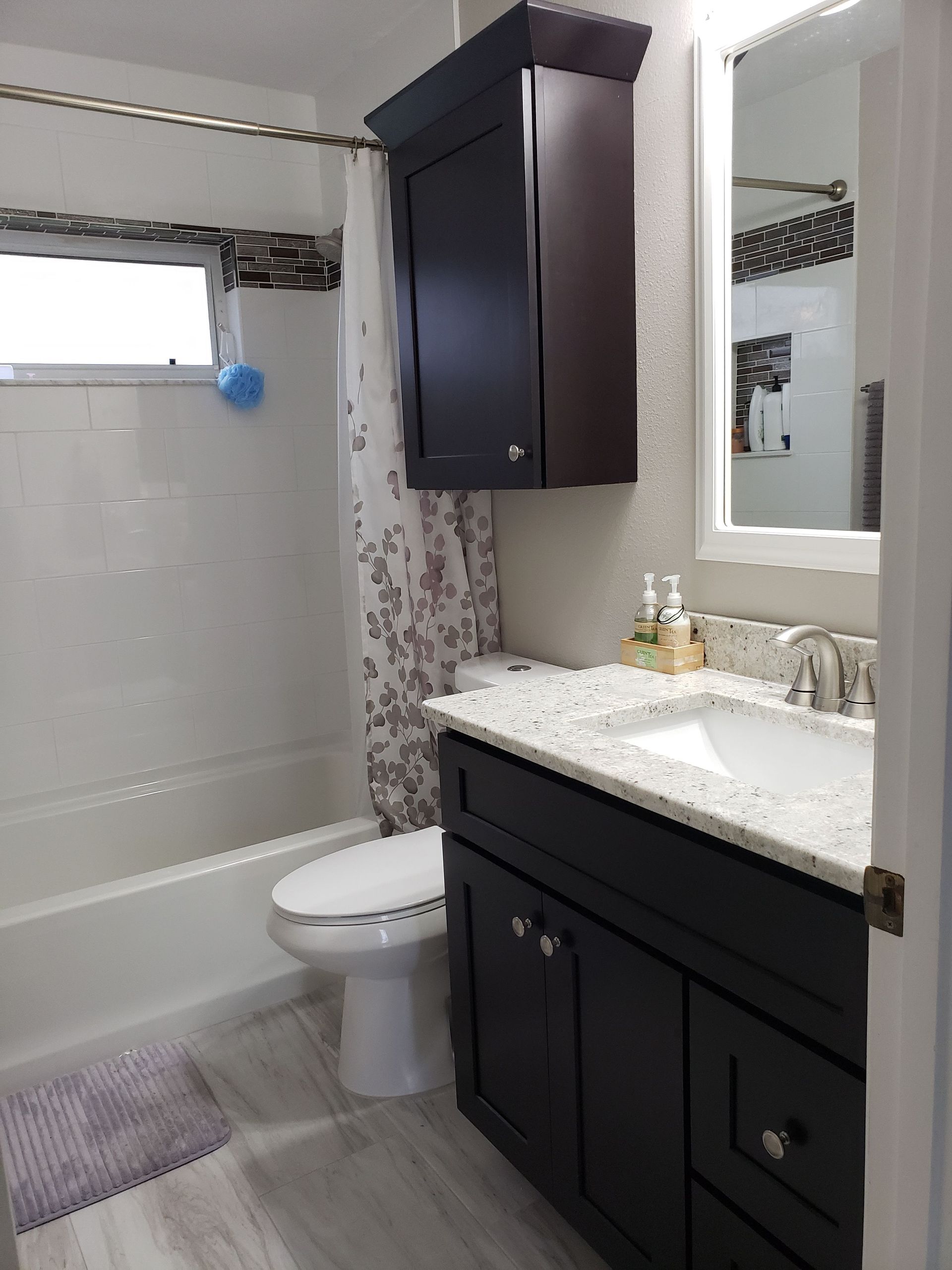 A bathroom with a white toilet, shower, speckled countertop, and dark wood vanity cabinets with a matching wall cabinet.