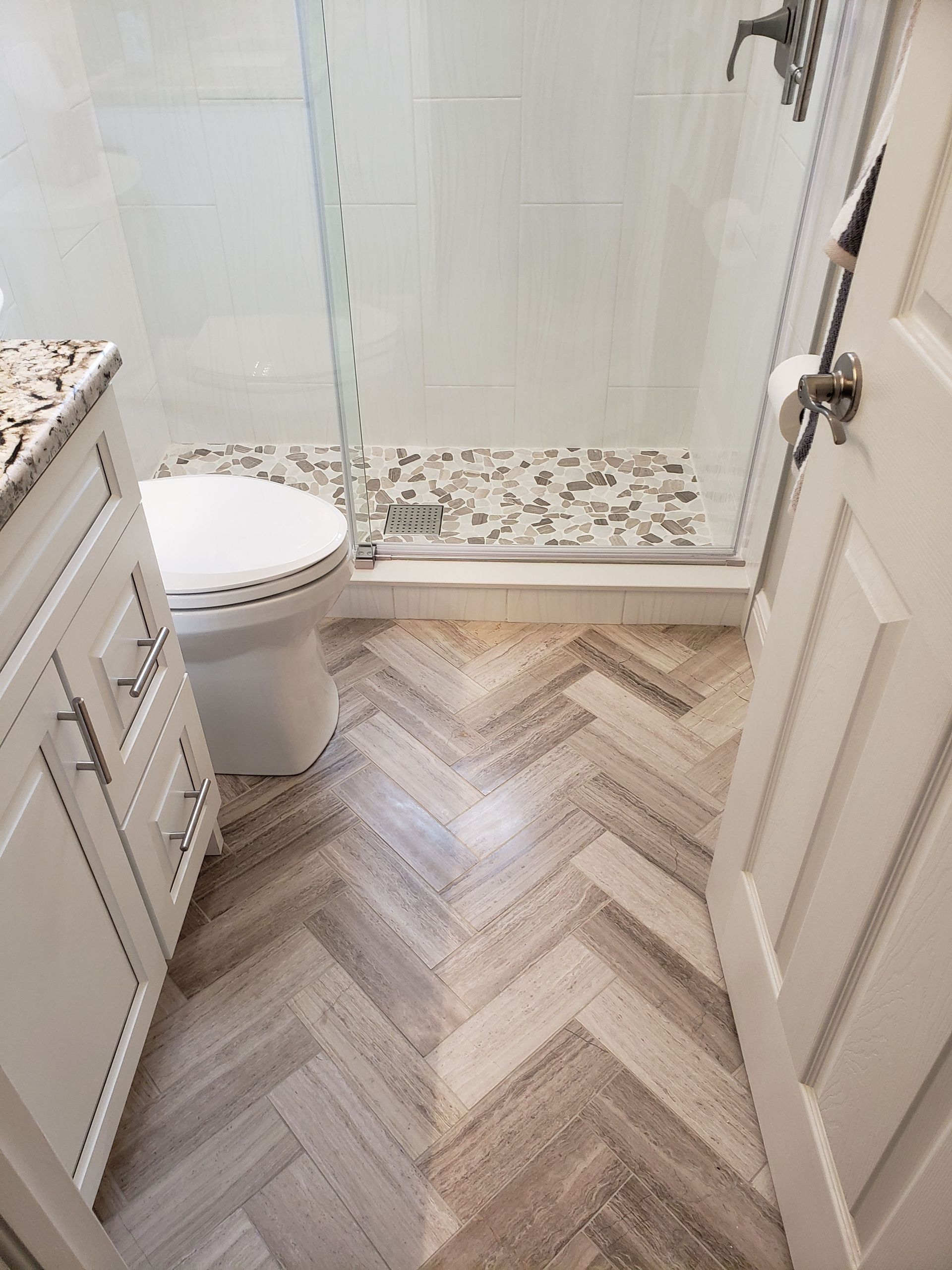 A bathroom view featuring light wood-look herringbone flooring, a white toilet, and a glass-enclosed shower stall.